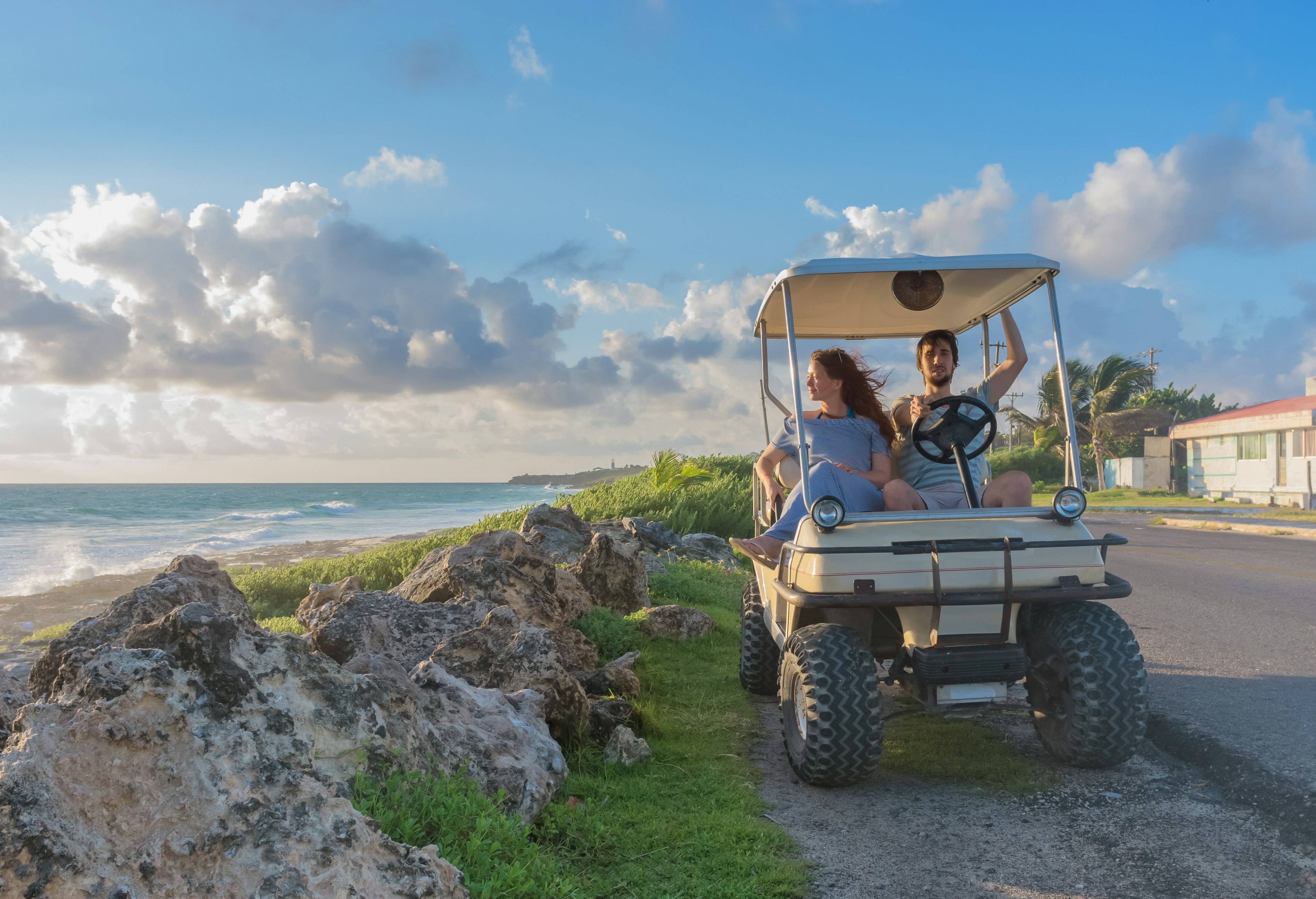 A young couple driving a golf cart alongside a tropical beach