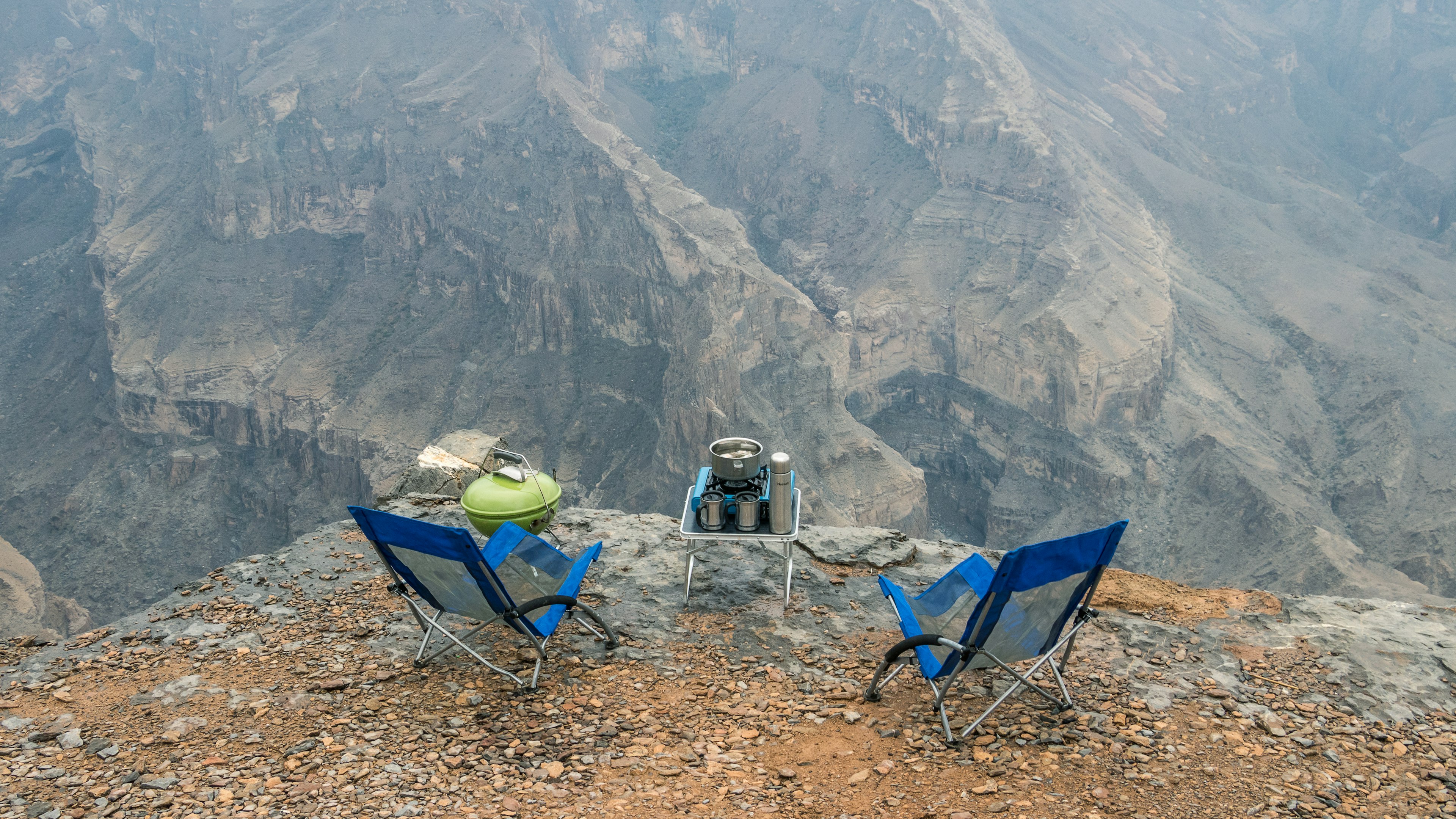 Two camping chairs and a camping stove on a steep cliff dropping off to a wadi in Jebel Shams, Oman