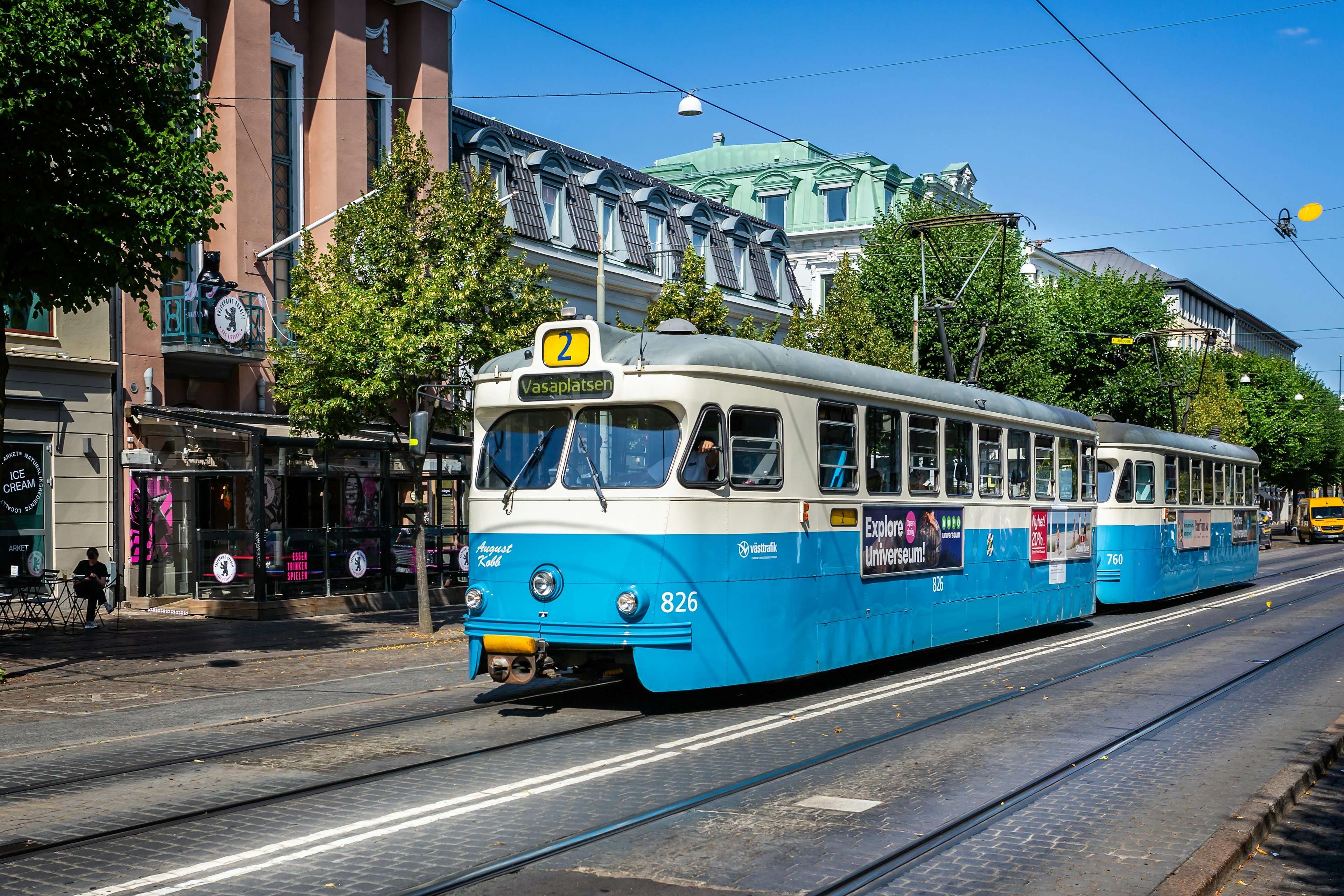 A blue-and-white electric tram pulls in to a tram stop in Gothenburg, Sweden