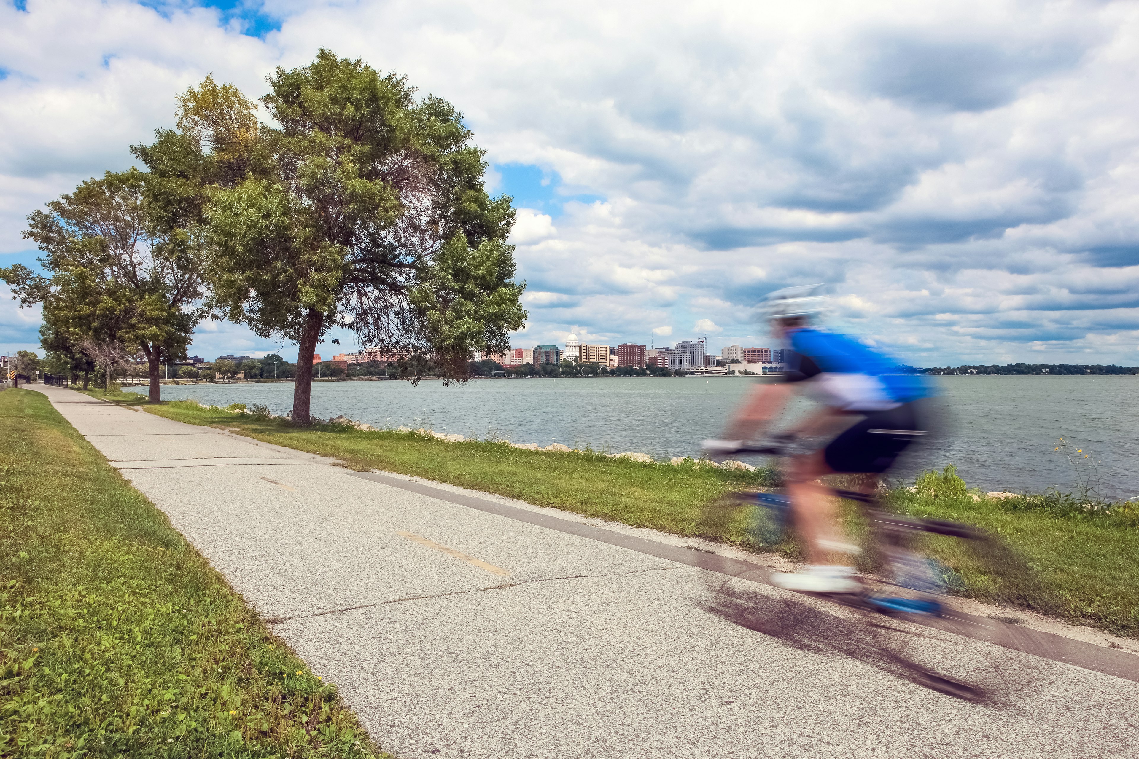 Motion blur of a person riding a bicycle on a lakeside bike path in Madison, Wisconsin with green trees and grass