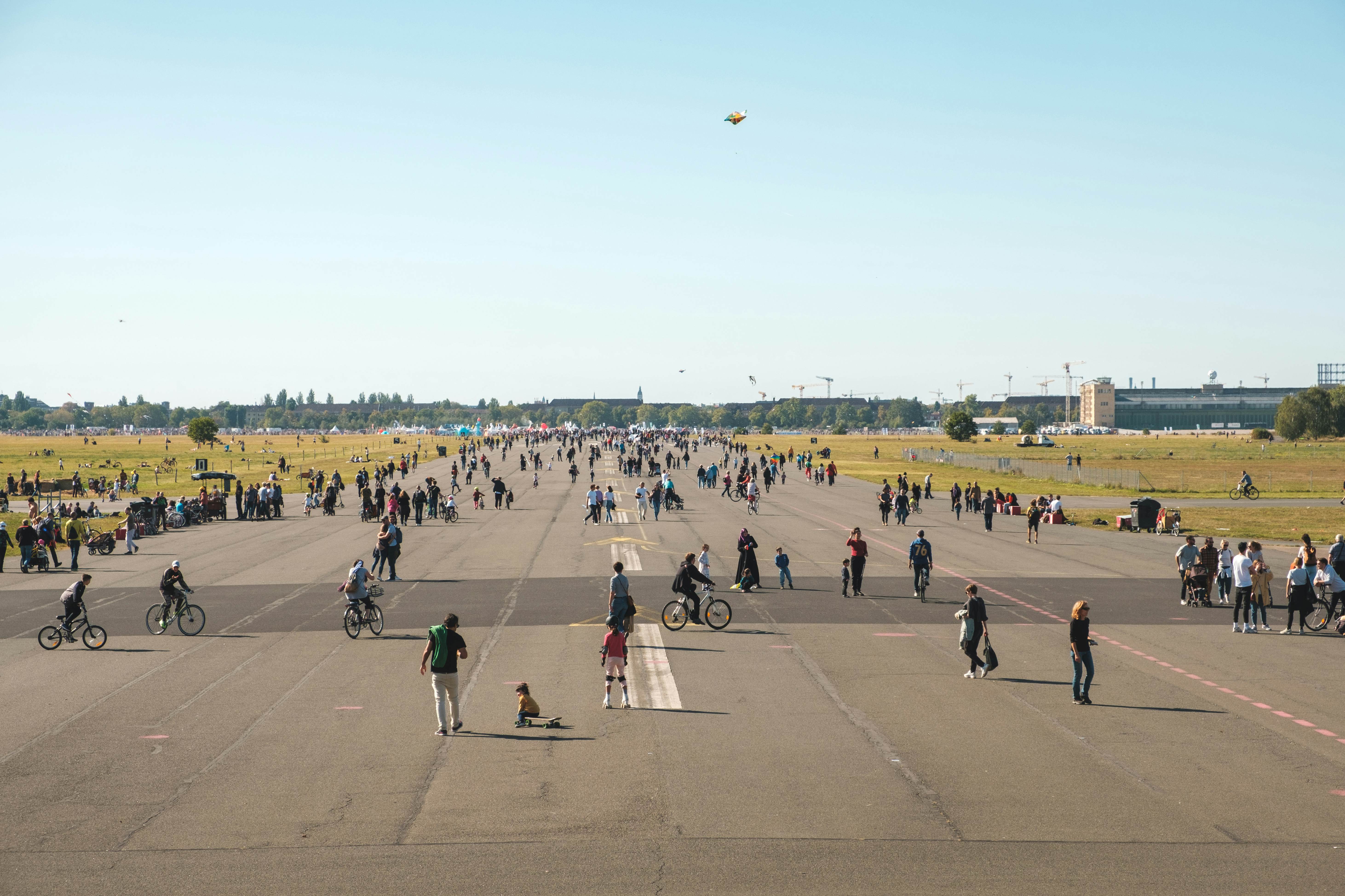 A former airport runway tuned into parkland, being used by people to fly kites, skate and ride bikes