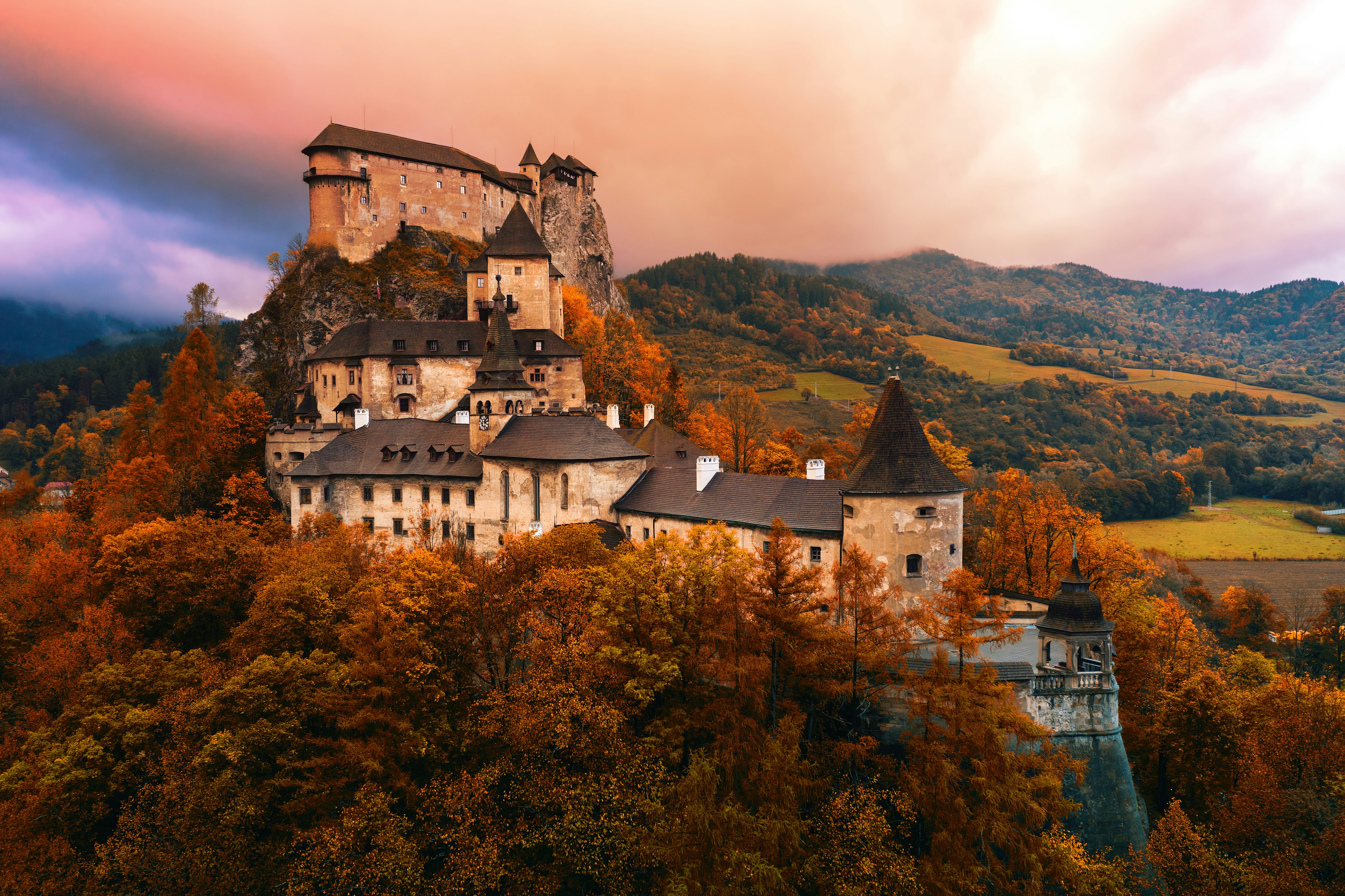 A large castle fortress on the top a hill surrounded by trees with golden brown leaves