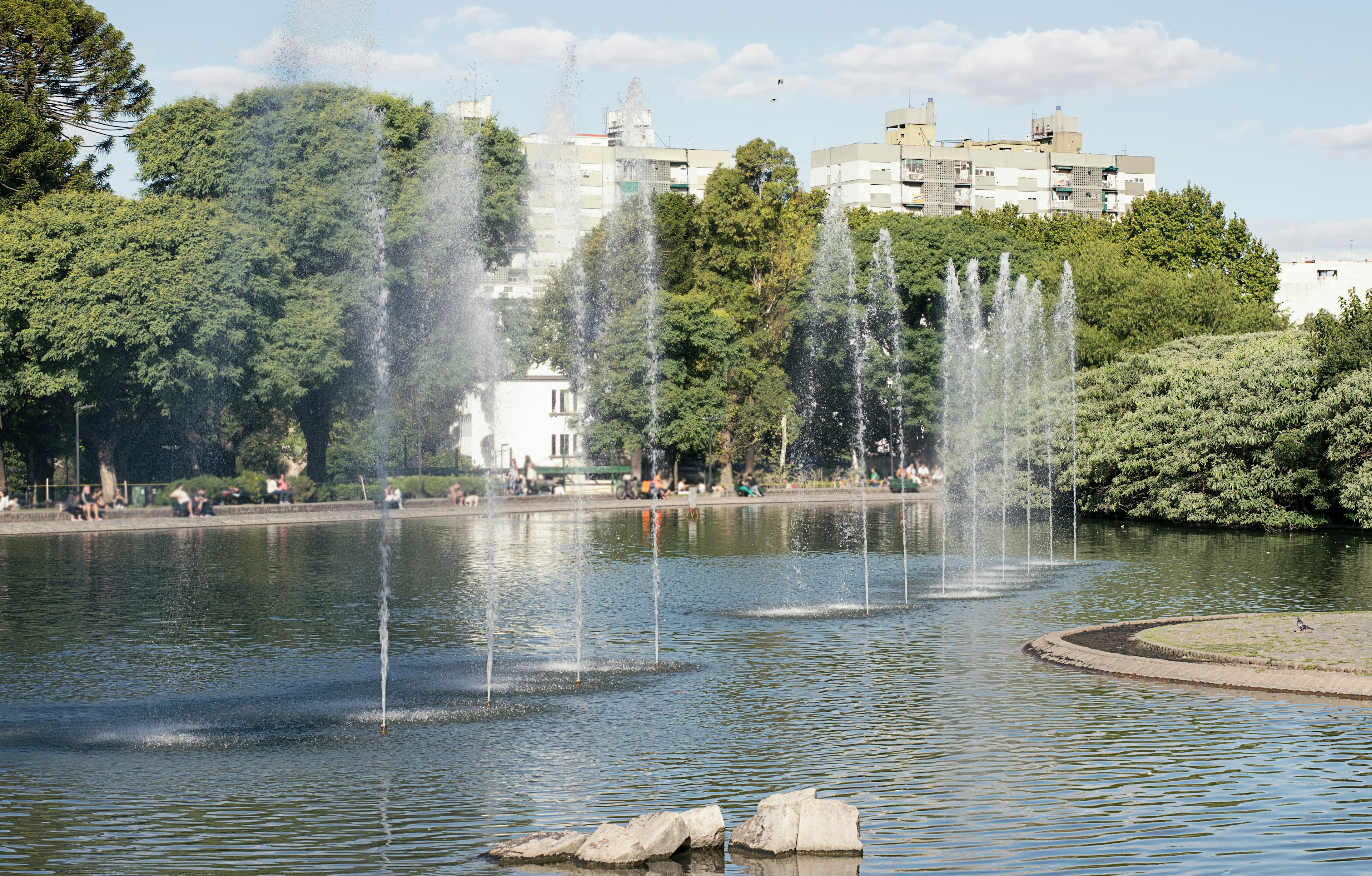 A large artificial lake with fountains; people are milling around in the surrounding park