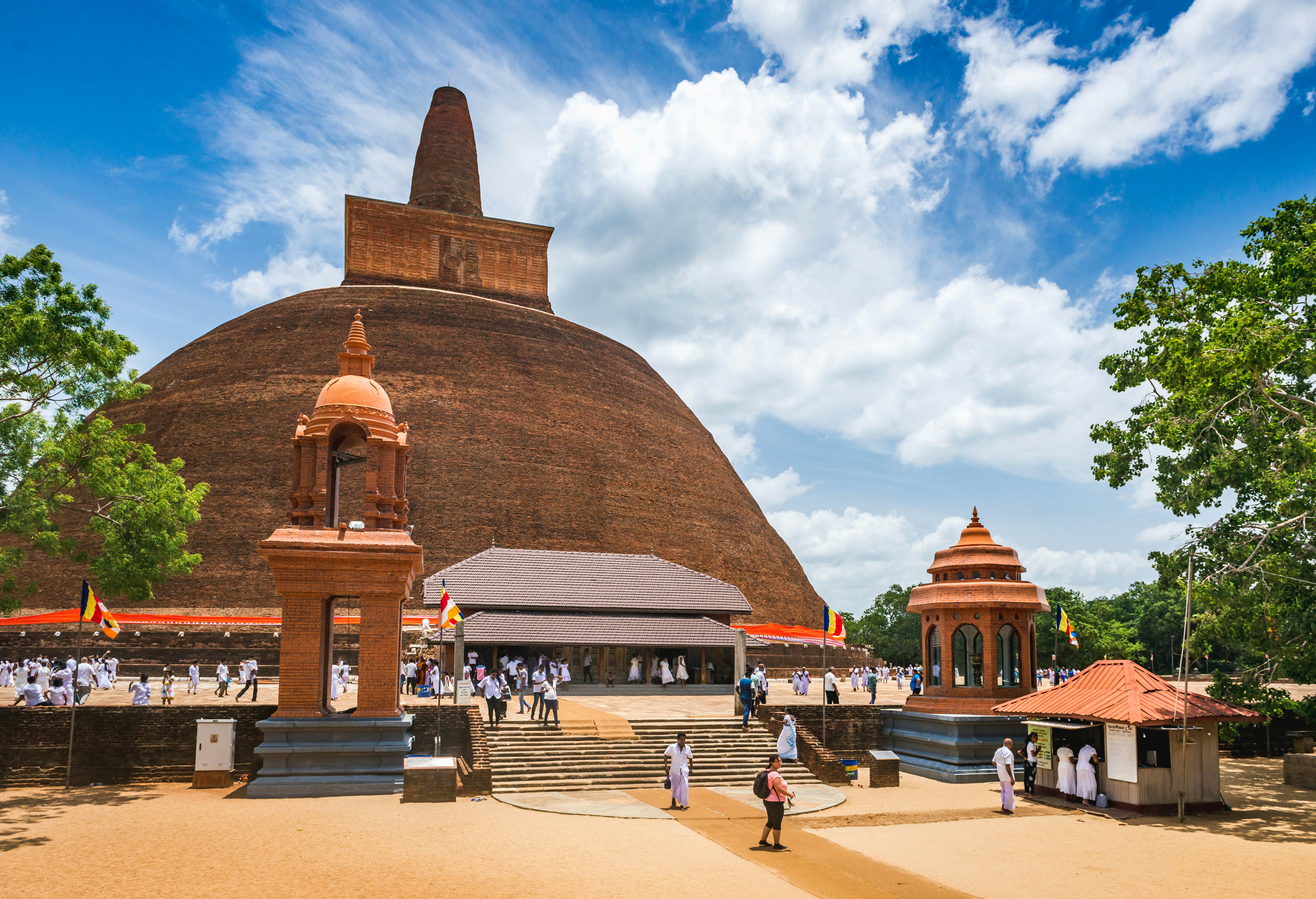 People walk near a vast brick stupa forming a dome shape with a pointed top