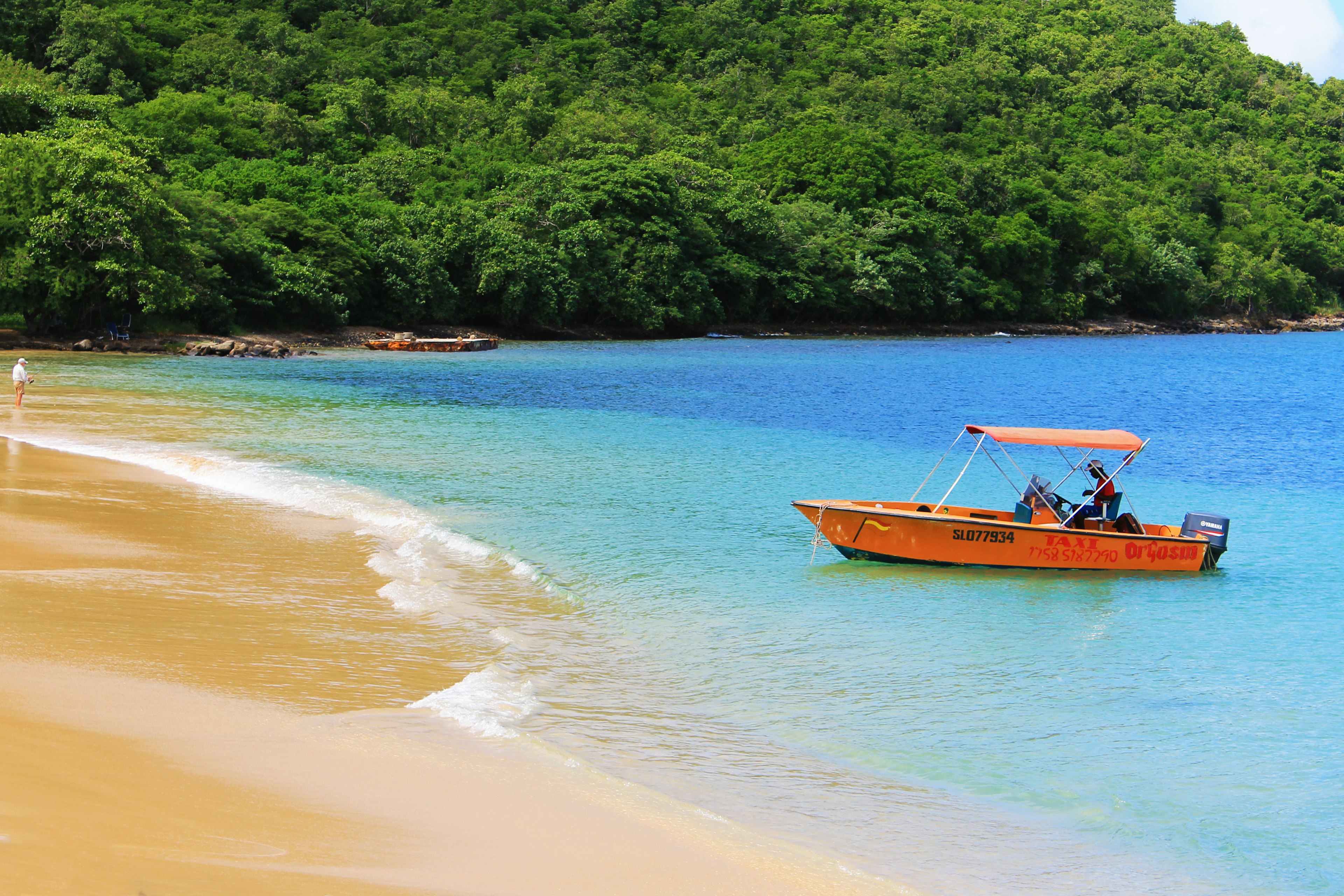 A small orange boat on approach to a golden sand beach