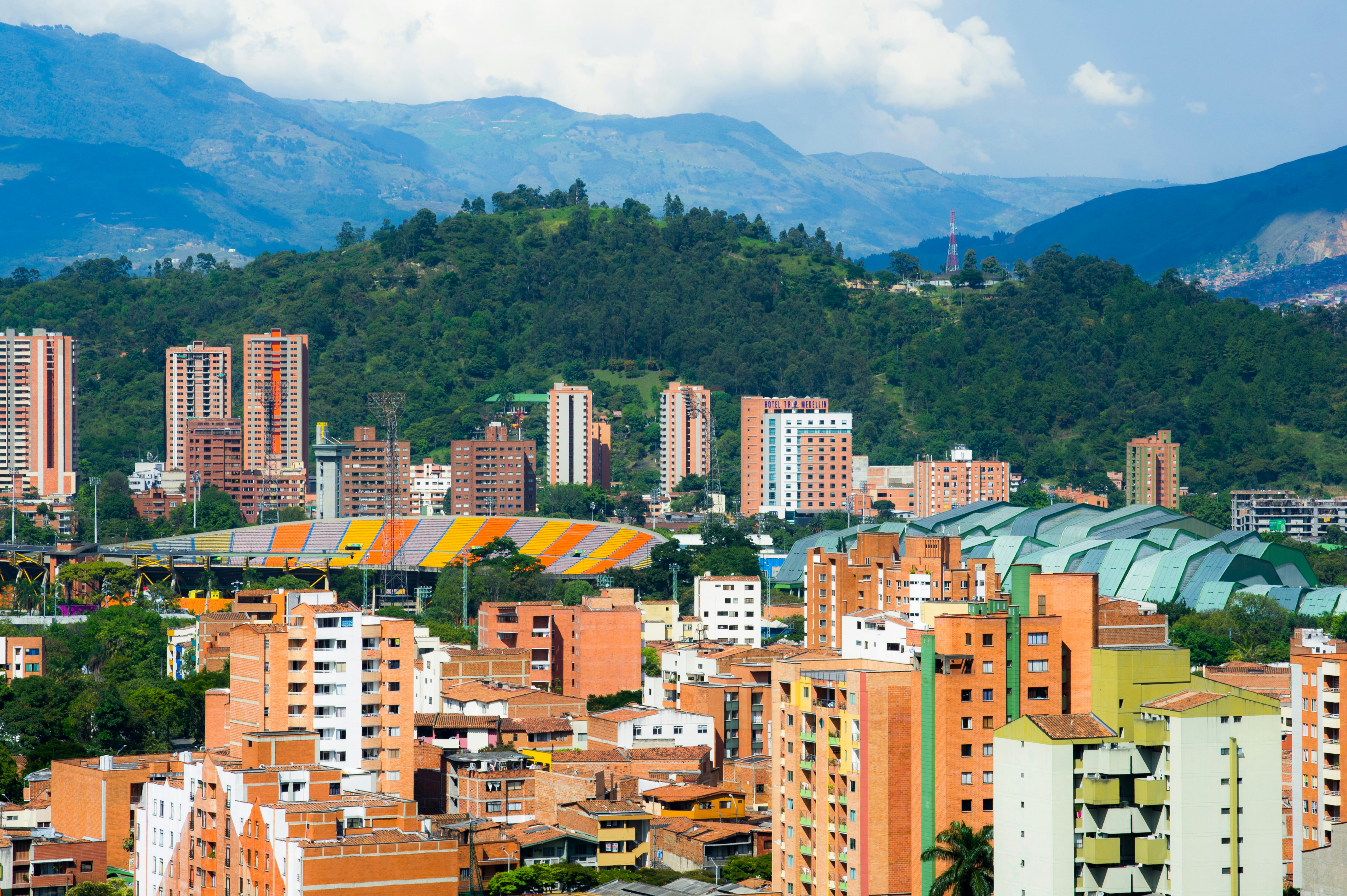 The roofs of a sports complex and a stadium pop out above the trees in a built-up area with red-brick high-rises