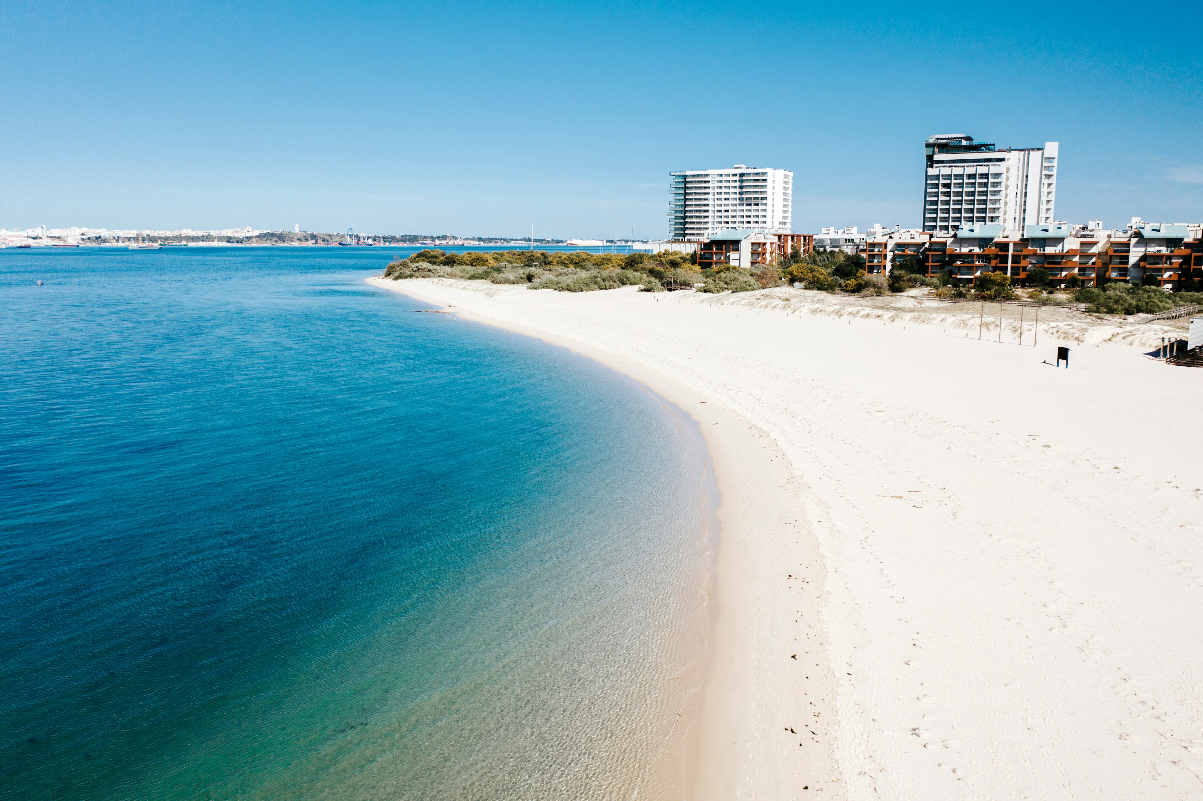 White sands meet a calm turquoise ocean, with large hotel buildings in the distance