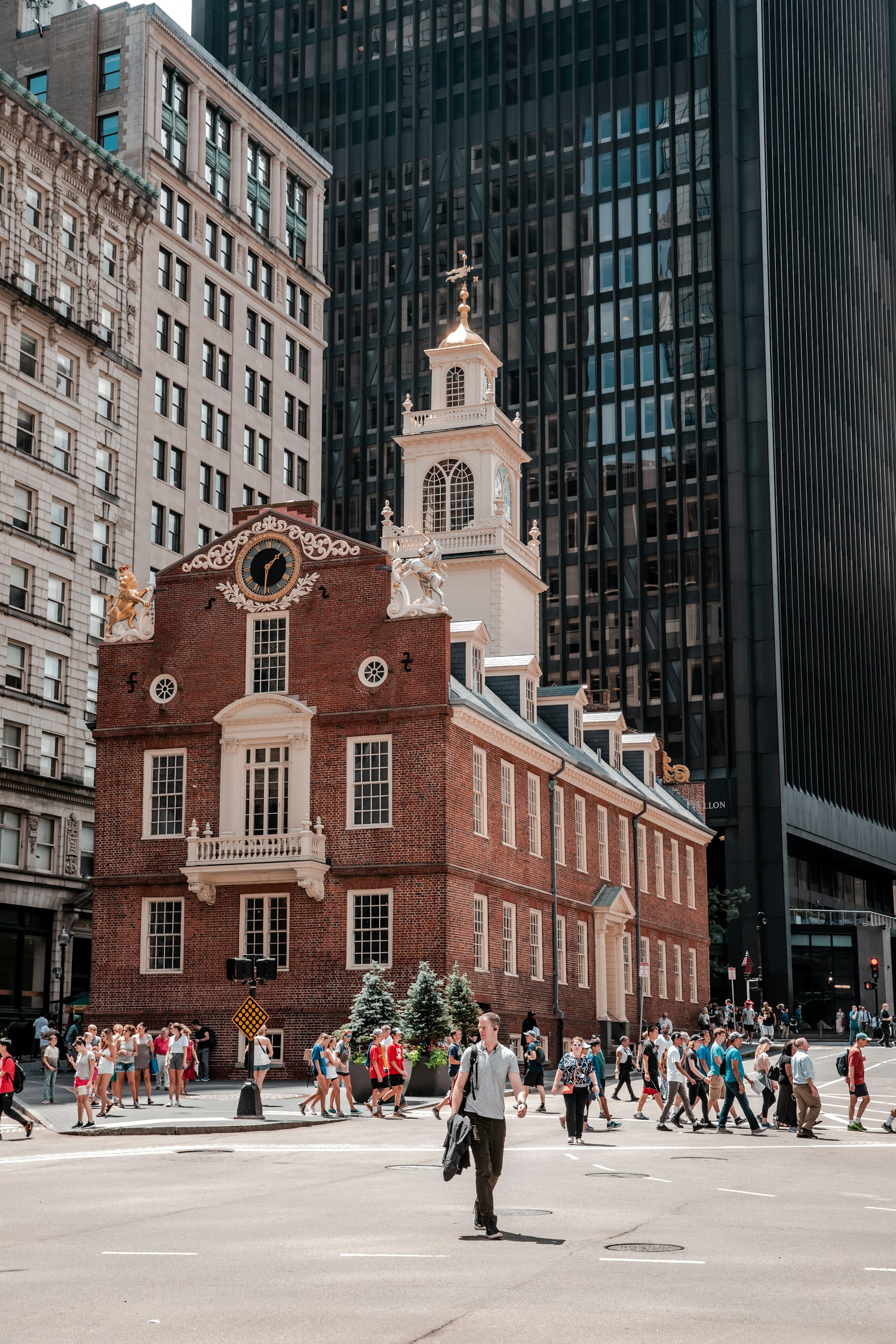 A redbrick building with a white tower at a busy city junction is dwarfed by taller buildings 