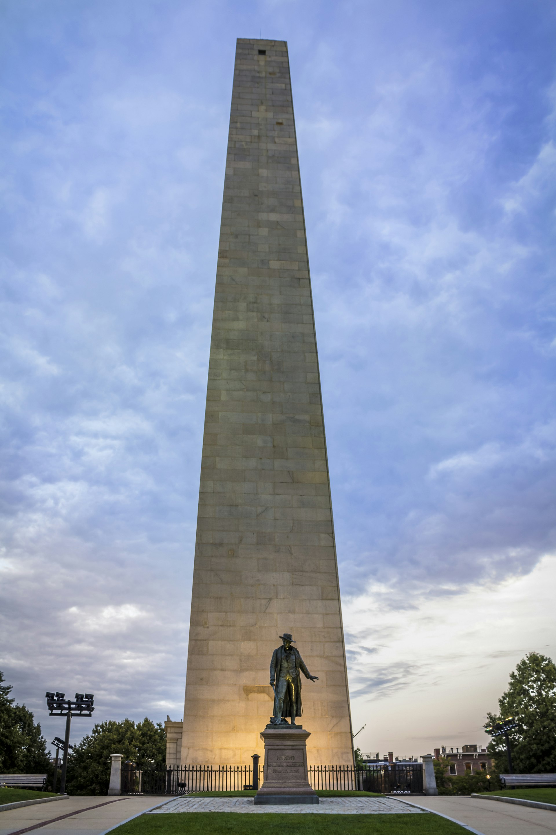 A tall stone obelisk with a statue of a man in front of it at sunset