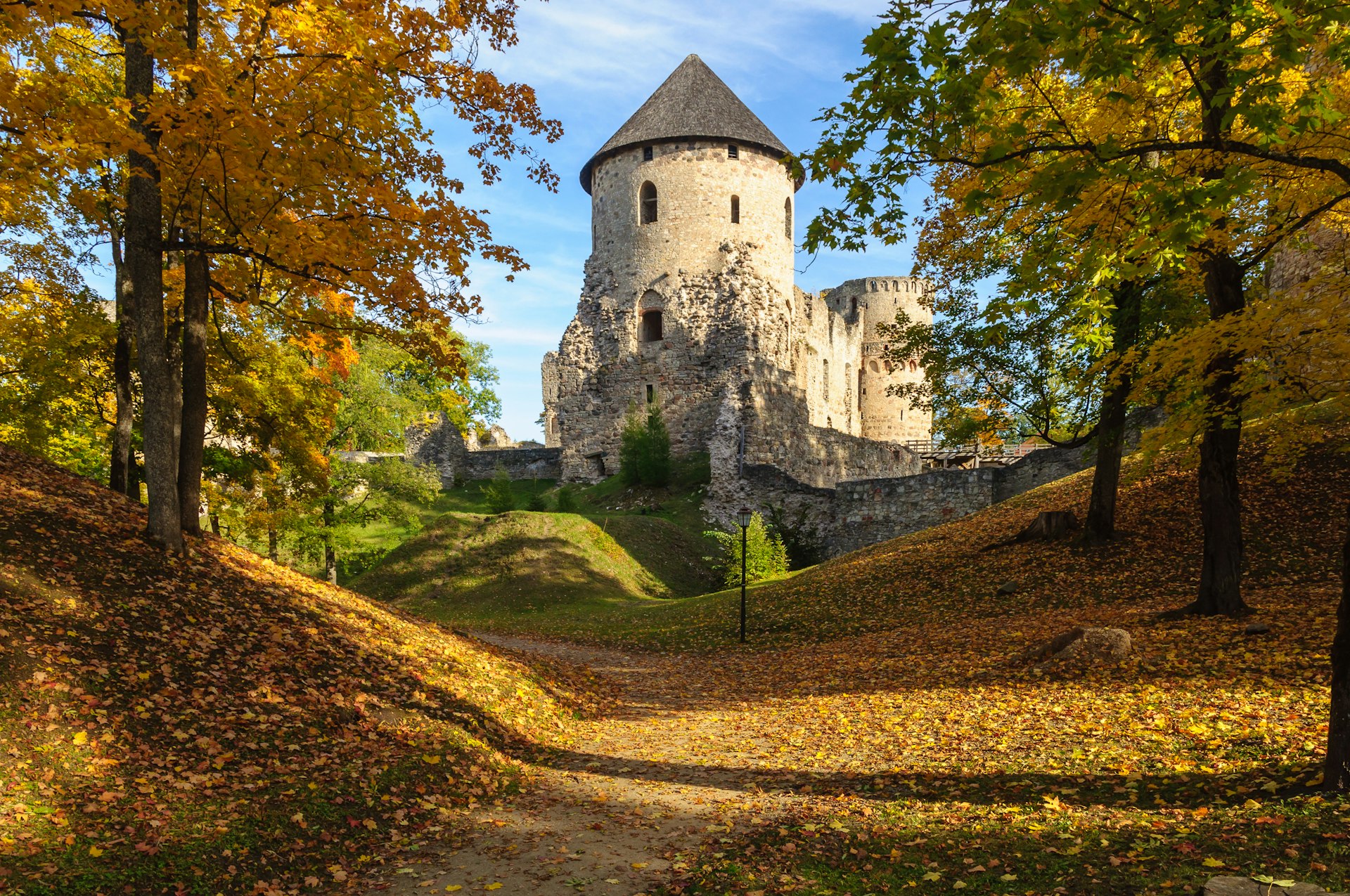 Medieval castle ruins sit in a forest where leaves are turning yellow in fall. 