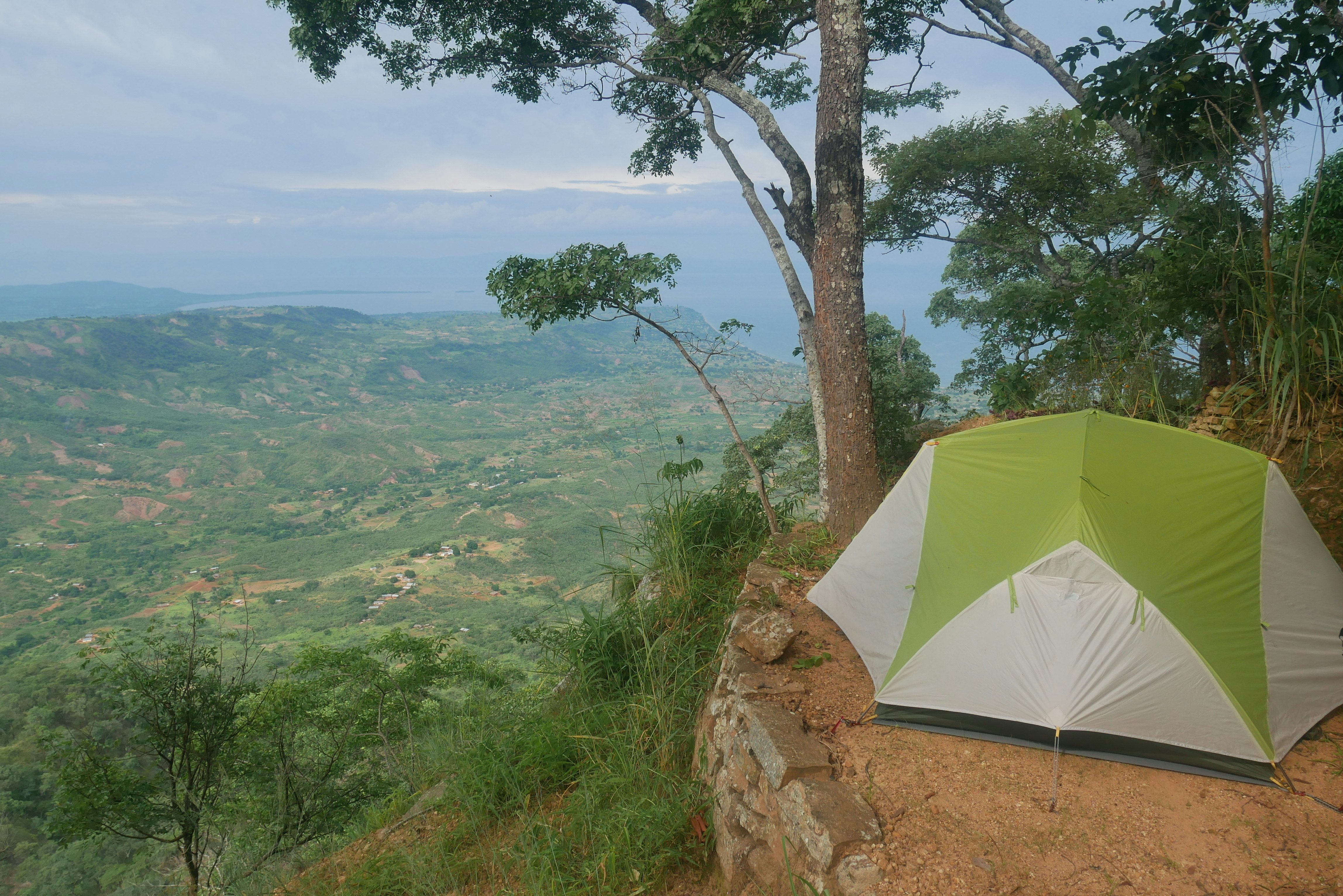 A tent perched on the edge of an escarpment with rural hilly views stretching to a lake in the distance