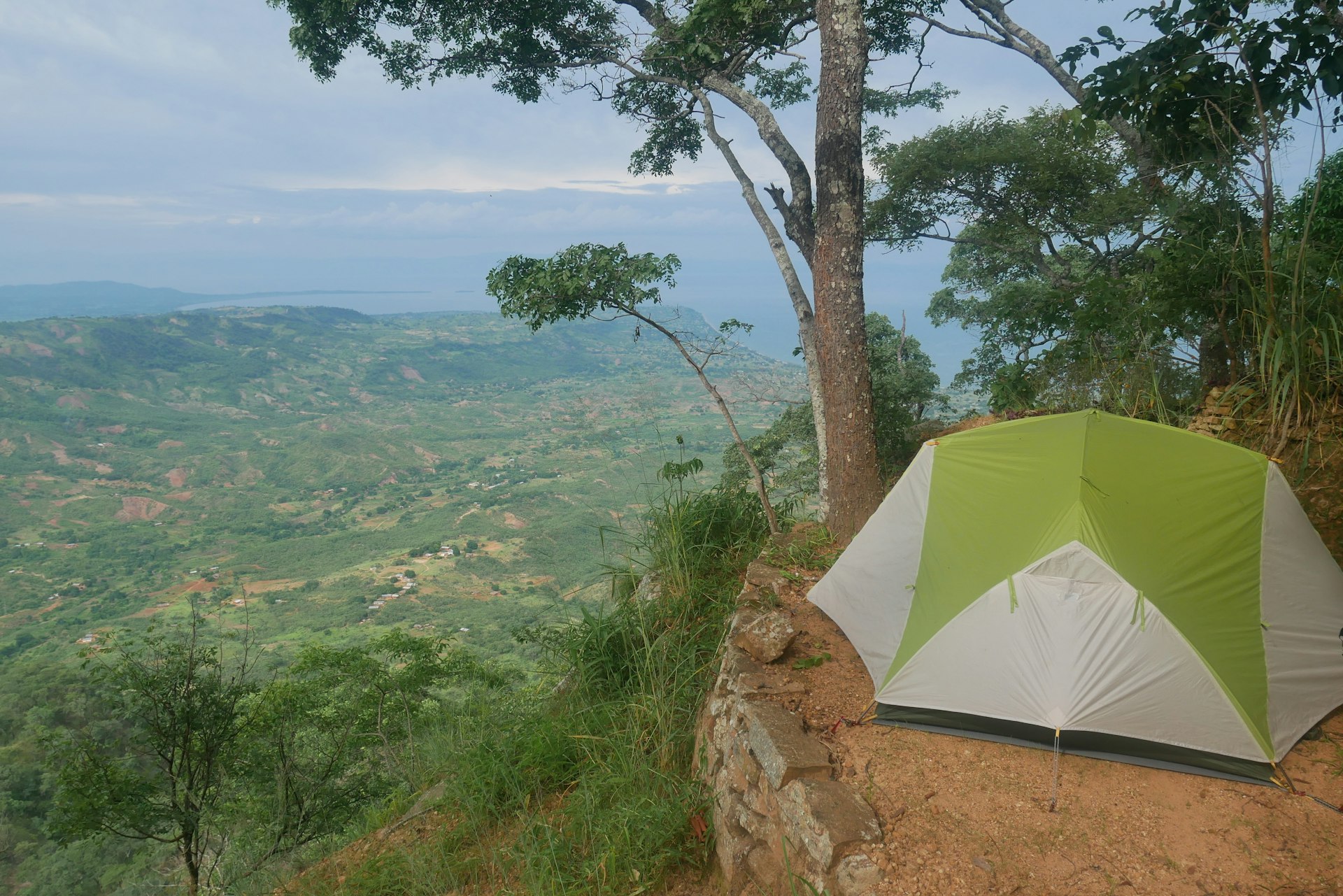 A tent perched on the edge of an escarpment with rural hilly views stretching to a lake in the distance 