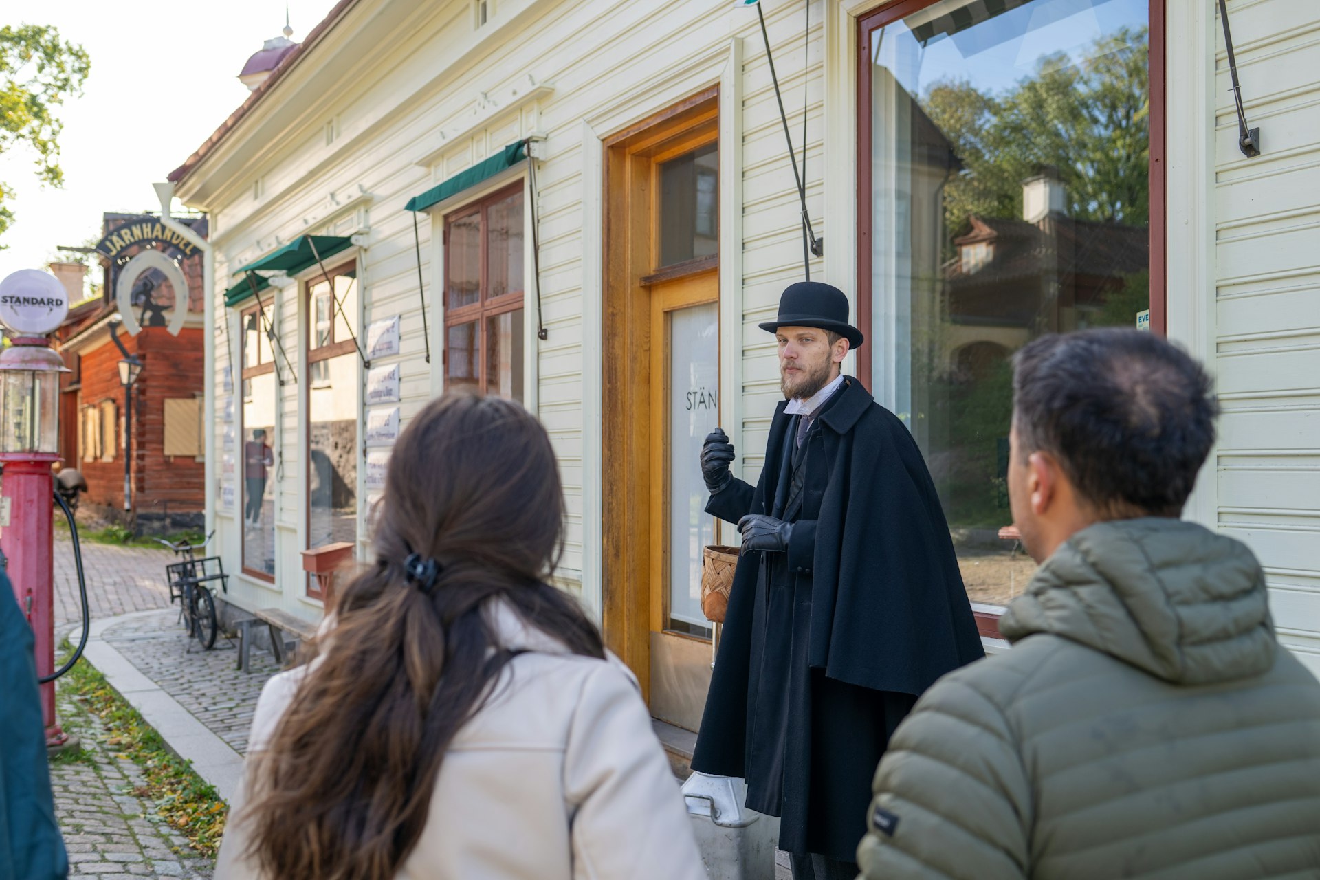 An guide in historical costume leads visitors through historic buildings in Skansen, an open-air museum in Stockholm