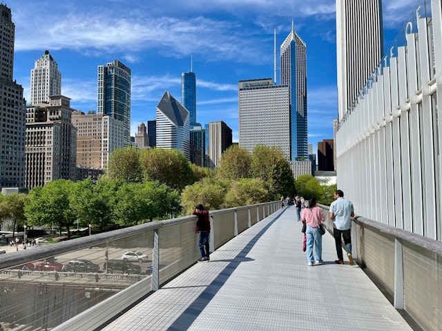 Several people walk along the elevated Nichols Bridgeway pedestrian bridge, which connects the Art Institute of Chicago with Millennium Park.