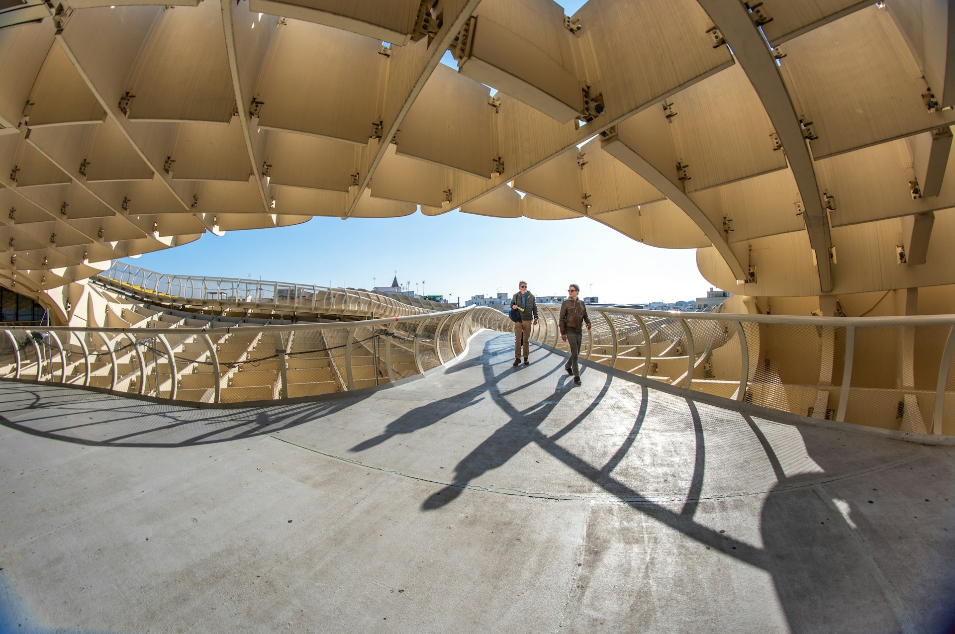 Two people walking on the iconic Las Setas (or Metropol Parasol) in Seville, Spain, under a clear blue sky