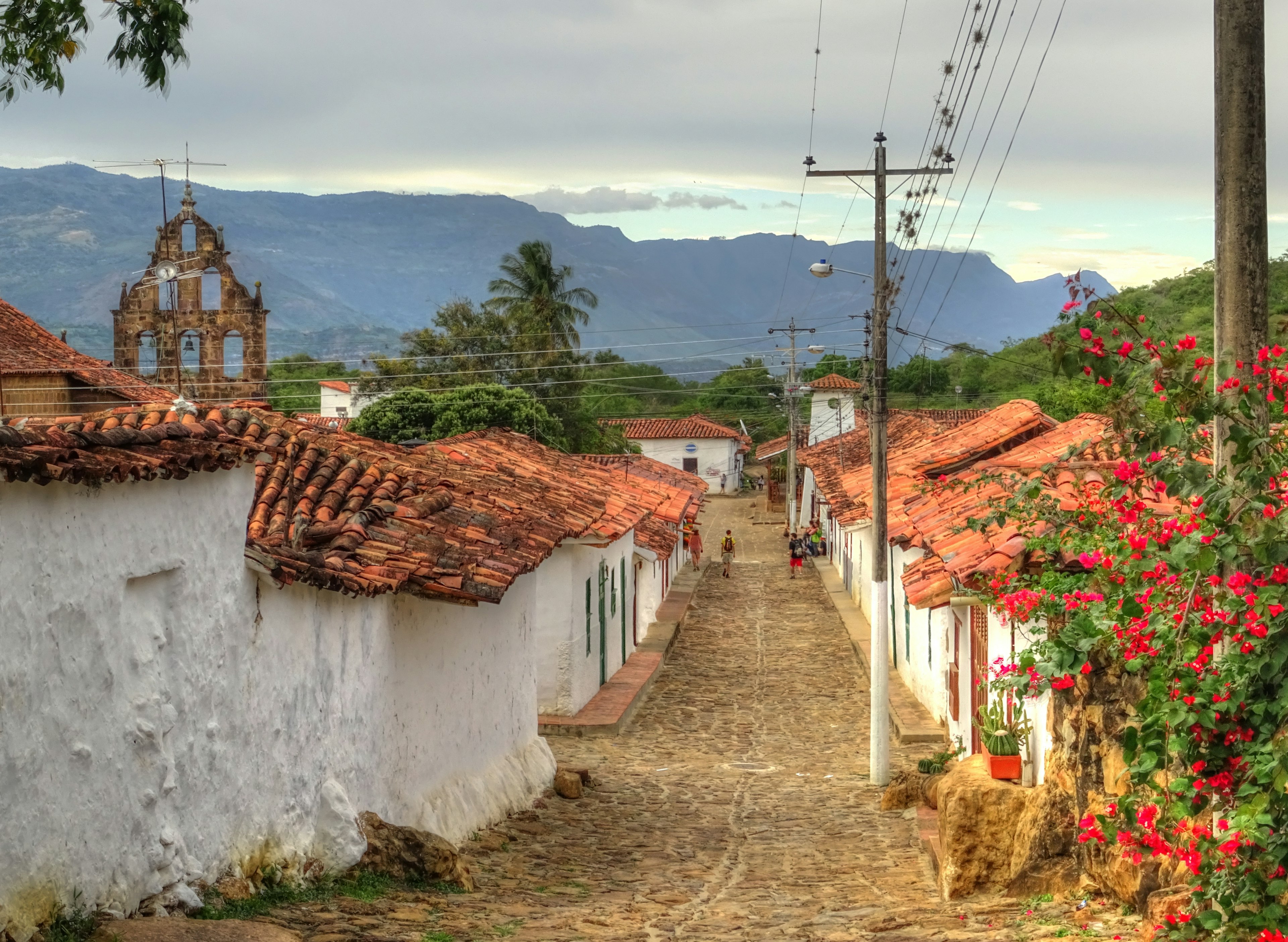 Trekkers follow a cobbled street through a village with low-rise whitewashed buildings with red tiled roofs