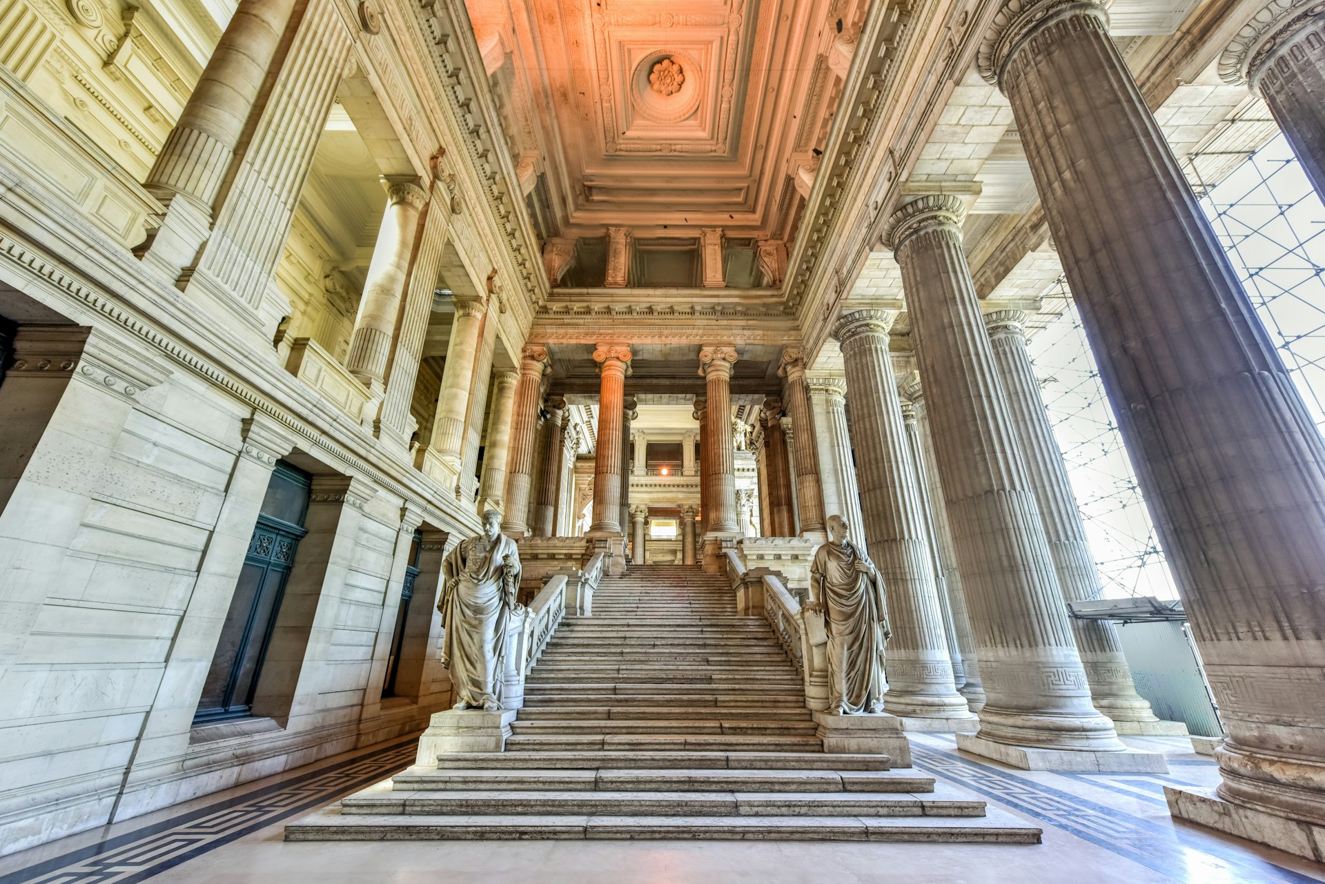 A marble stairway with imposing neoclassical columns and statues inside the Palais de Justice, Brussels