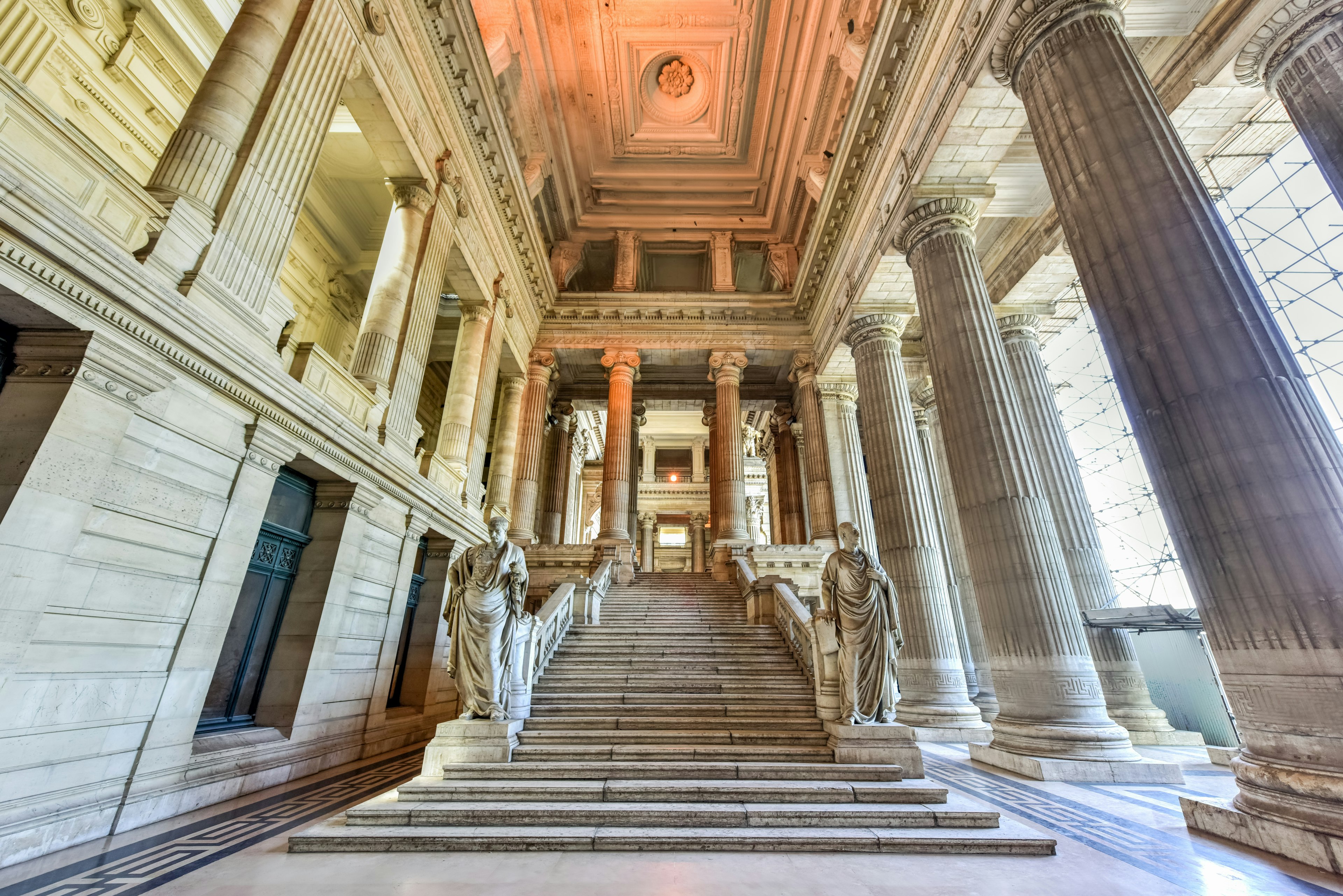 A marble stairway with imposing neoclassical columns and statues inside the Palais de Justice, Brussels