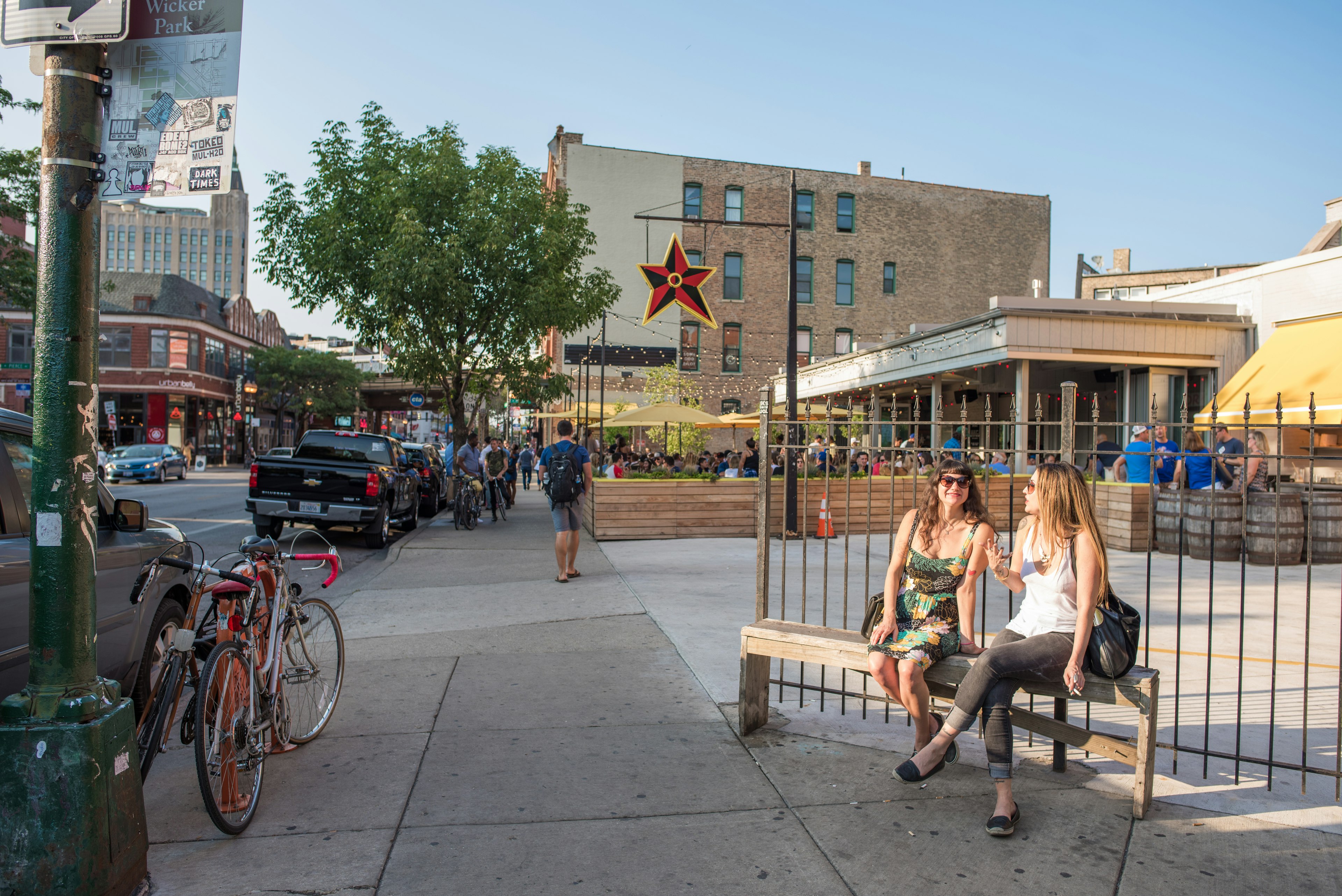 Two young women sit on a bench at the entrance to the restaurant Big Star in Chicago on a sunny evening