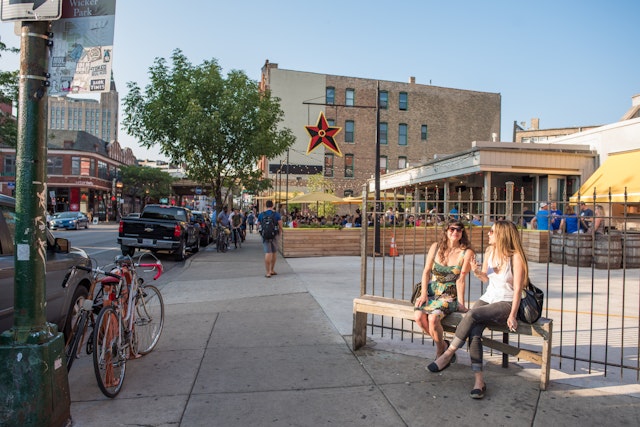 Two young women sit on a bench at the entrance to the restaurant Big Star in Chicago on a sunny evening