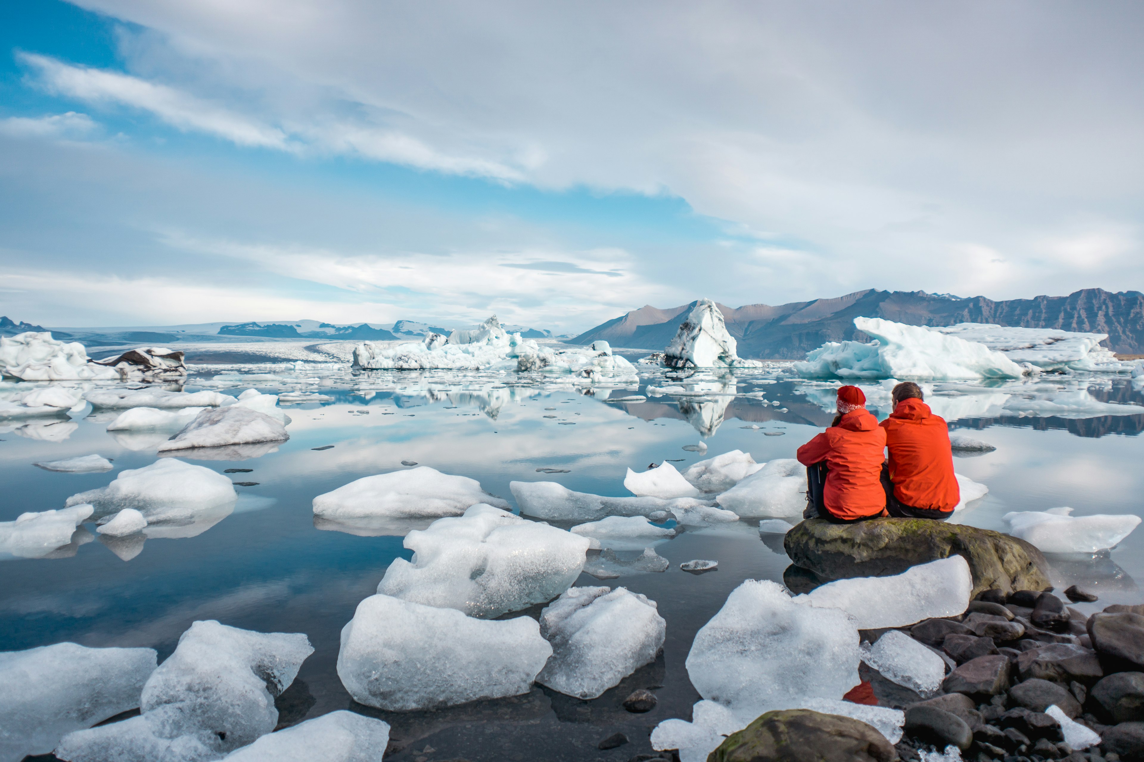 A couple sit on the edge of a lagoon filled with icebergs