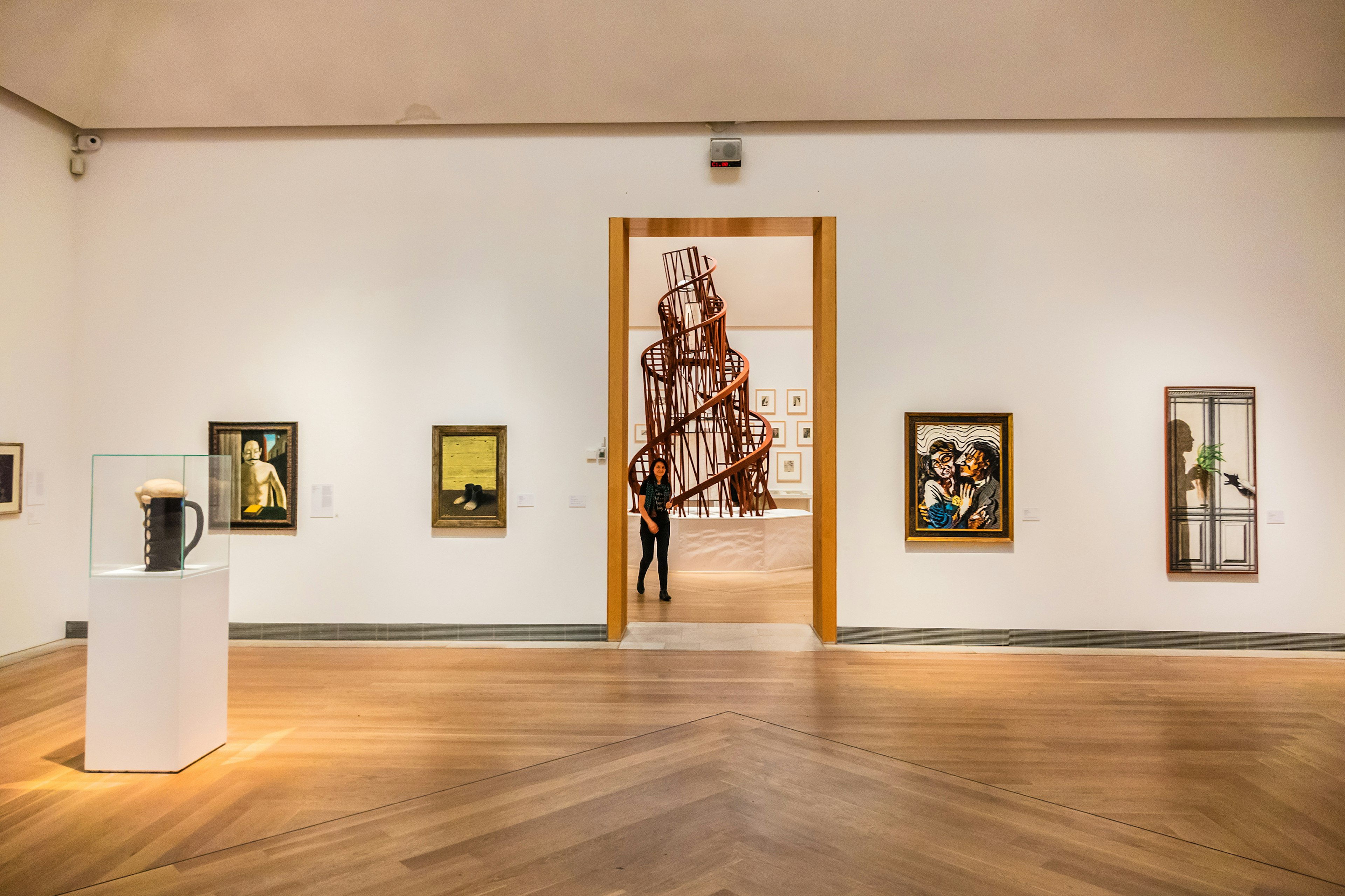 A gallery space with various pieces of modern art on the walls and a central spiral sculpture viewed through a doorway