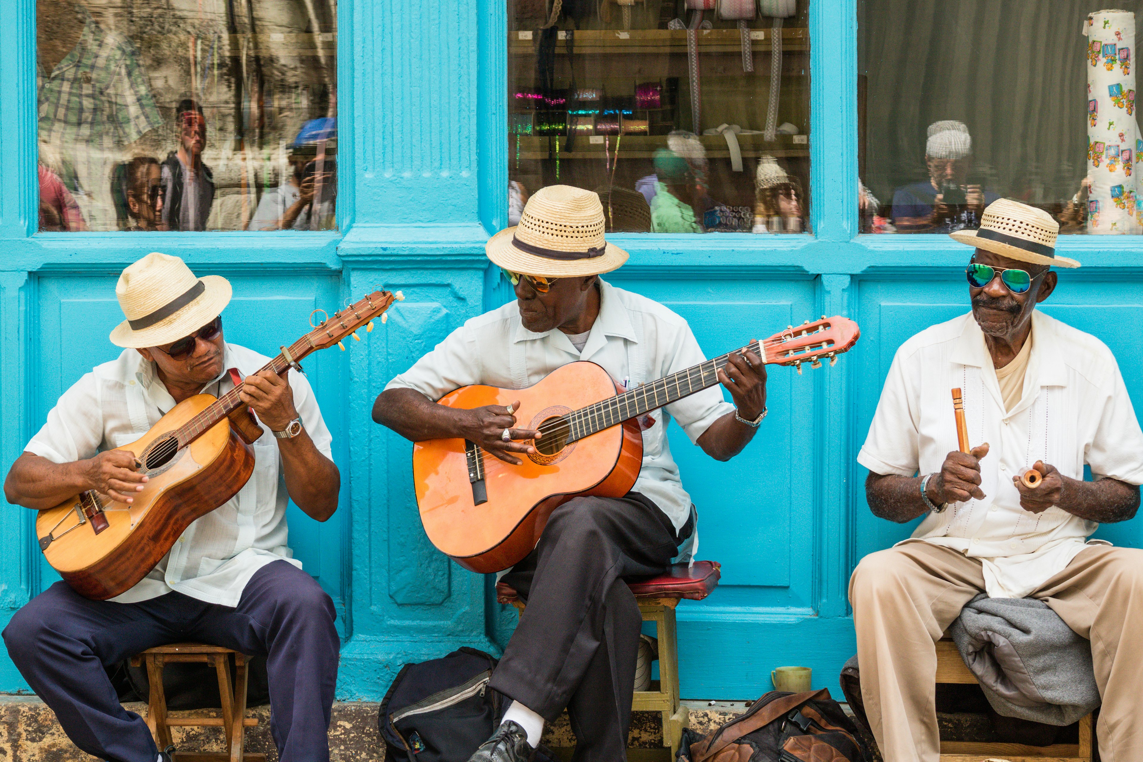 Three elderly musicians play guitars and percussion in a street performance