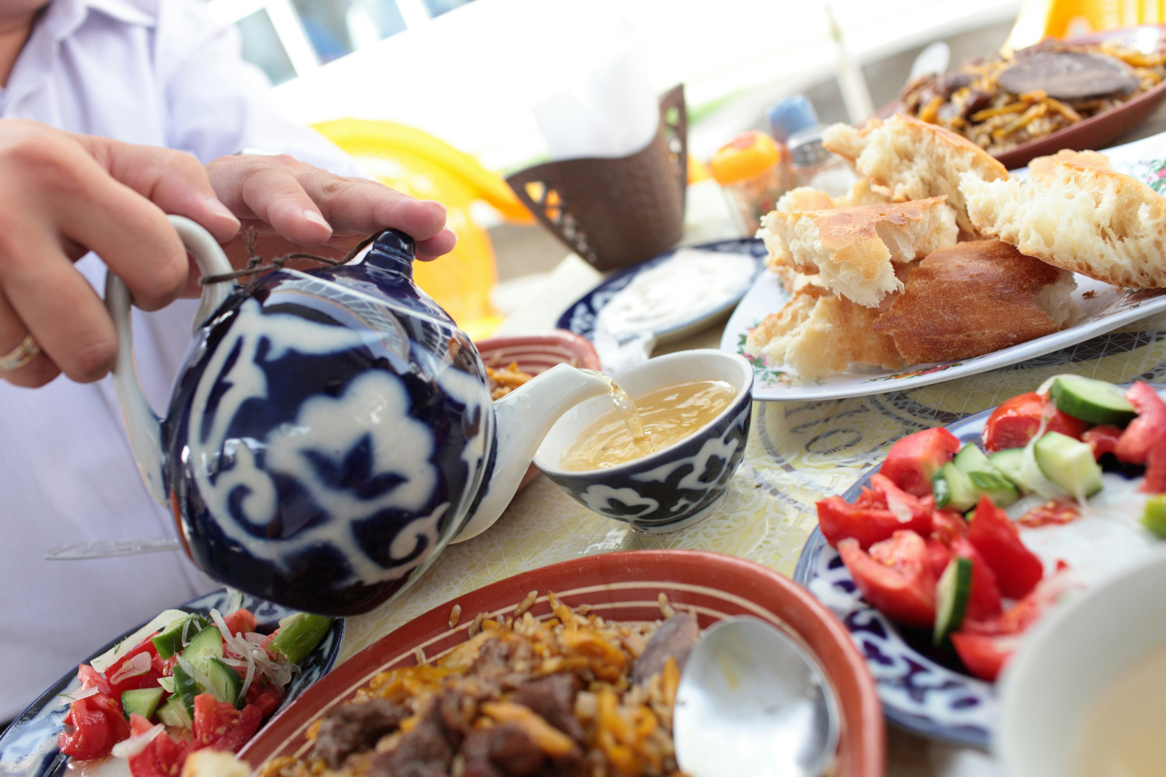 Man pouring green tea in uzbek restaurant at a table covered in plates of food