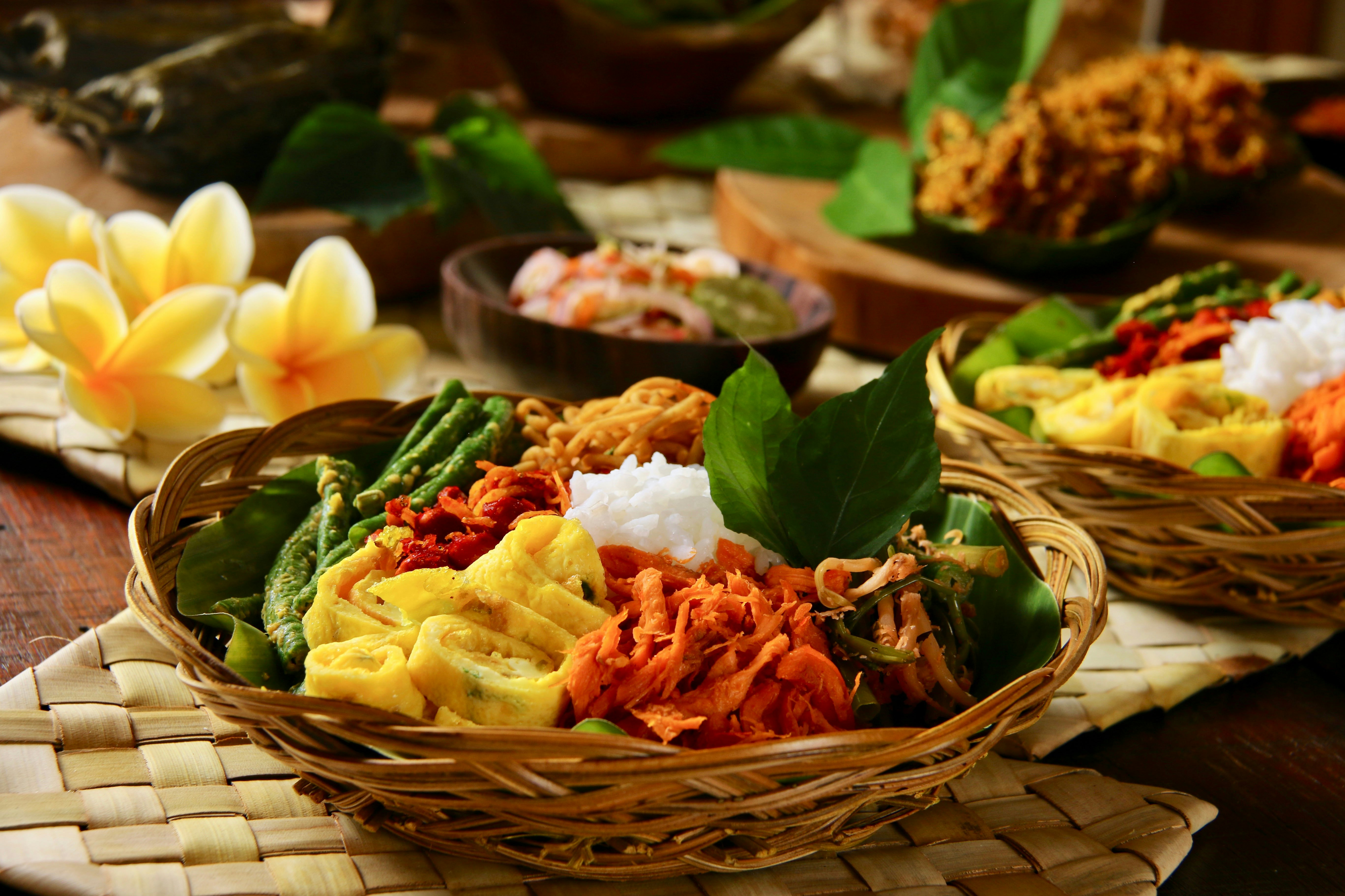 Nasi Campur Bali, a Balinese meal of rice with a variety of side dishes, shown in a wicker bowl near other food bowls