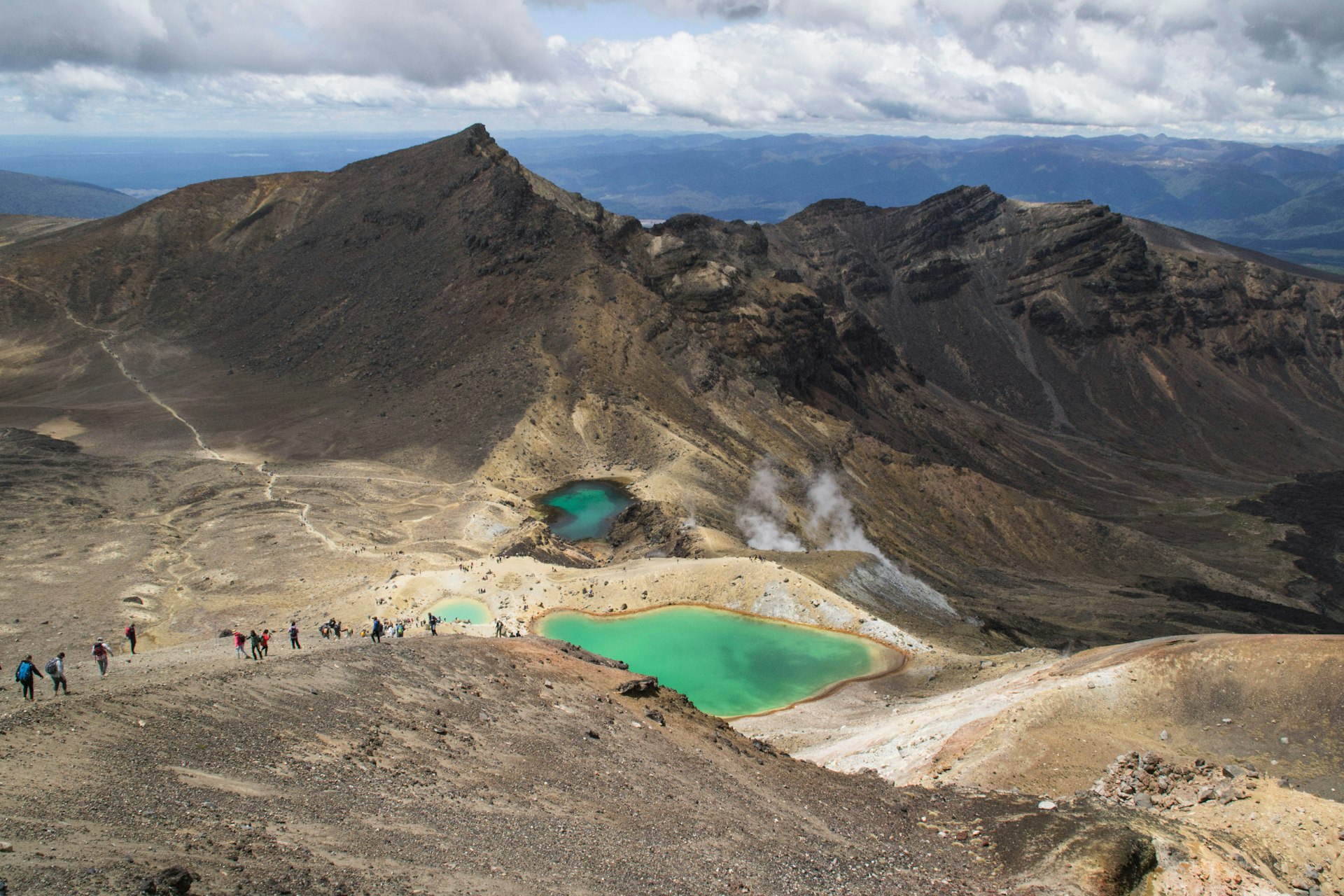 Hikers walk among volcanic landscapes and green lakes on the Tongariro Alpine crossing, New Zealand