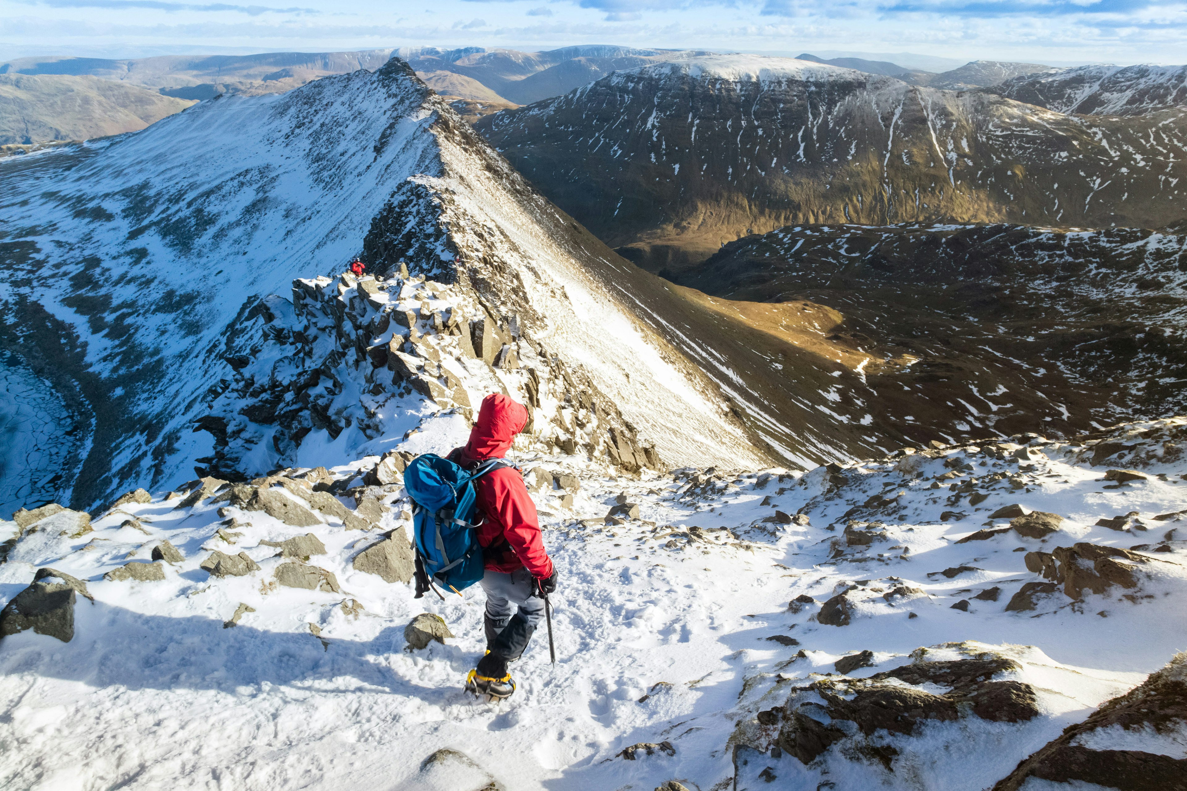 A hiker descending Helvellyn towards Striding Edge and Red Tarn in the Lake District