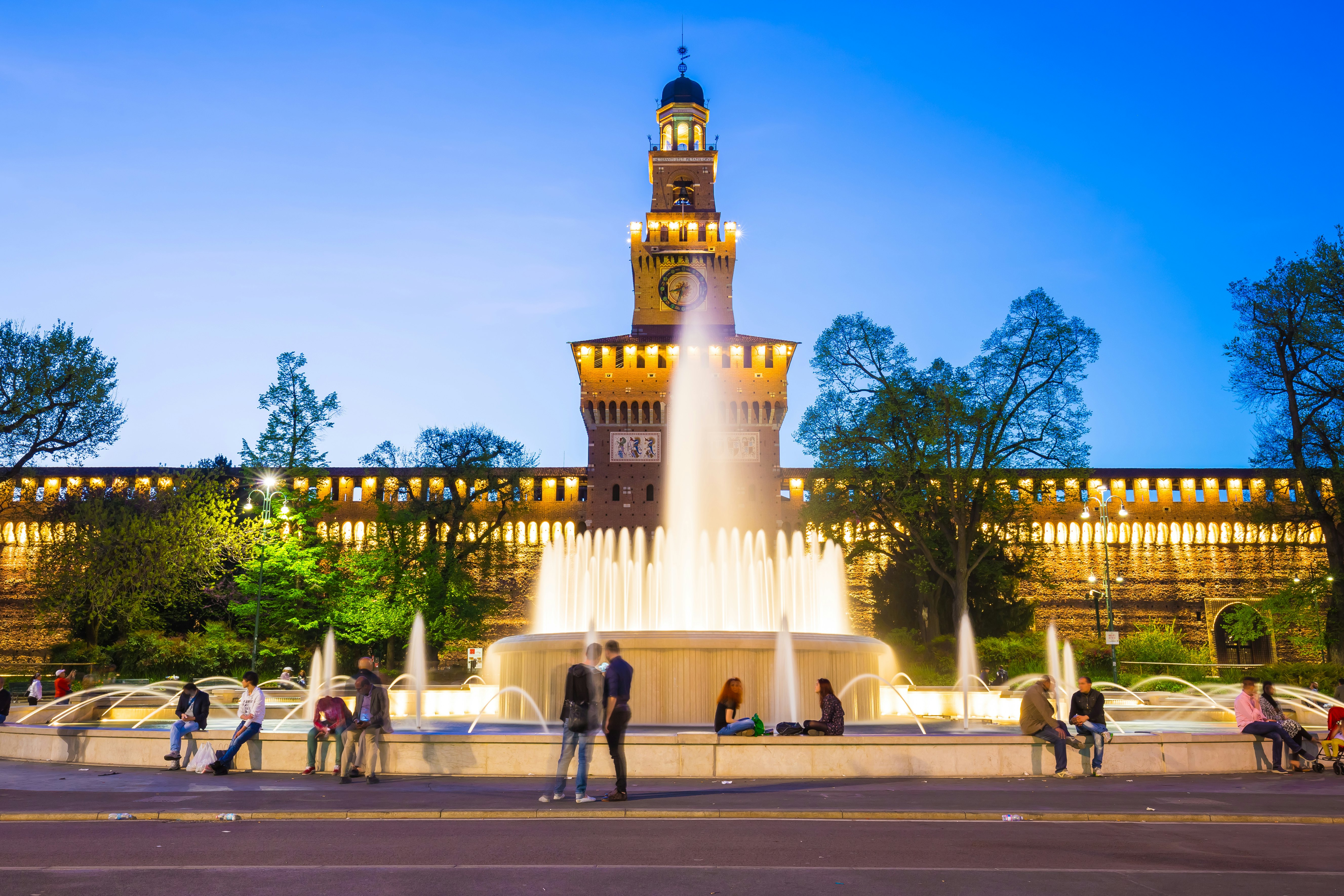 People sitting around a fountain in front of Sforza Castle (Castello Sforzesco) at night