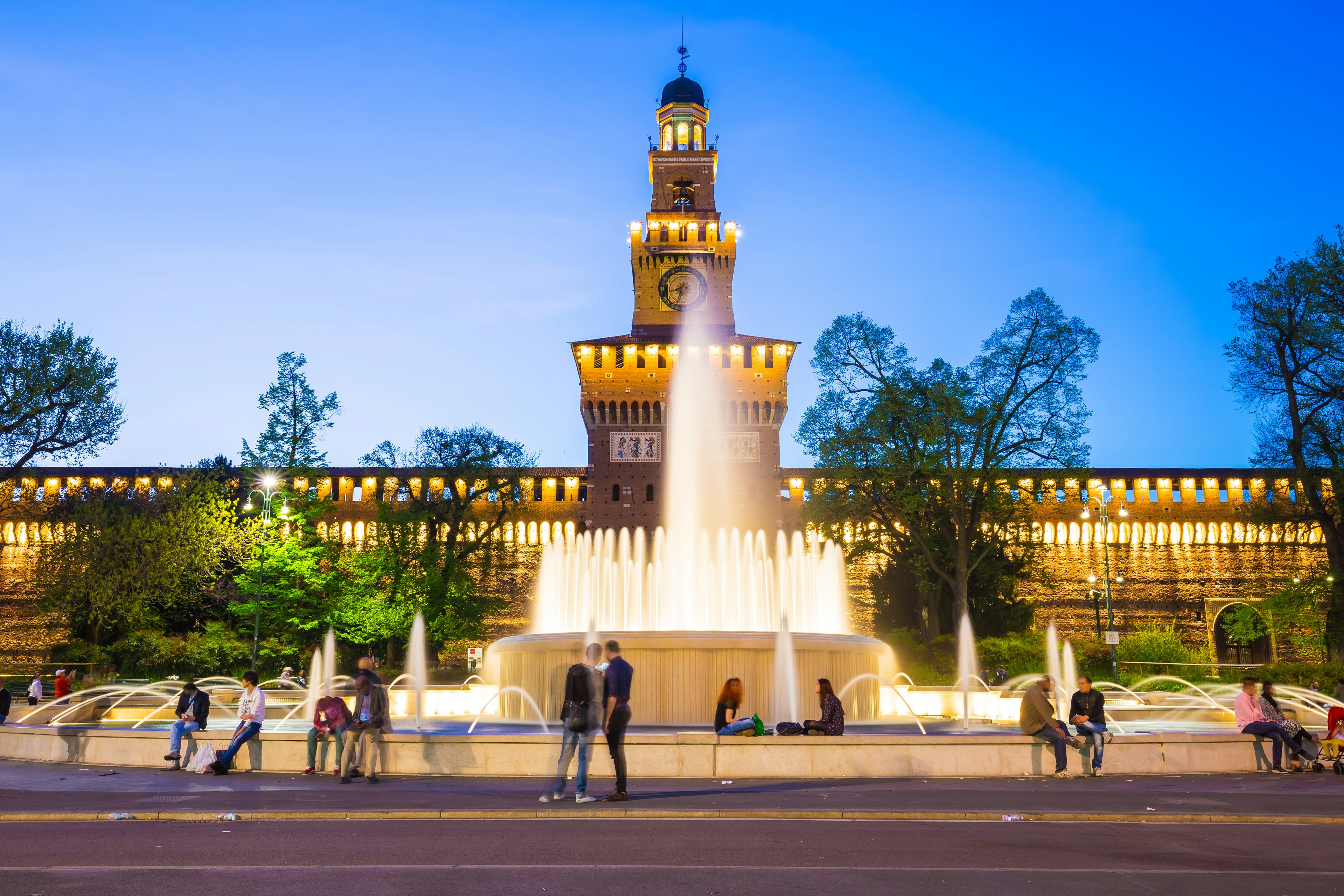 People sit around a fountain in front of Castello Sforzesco in Milan, Italy