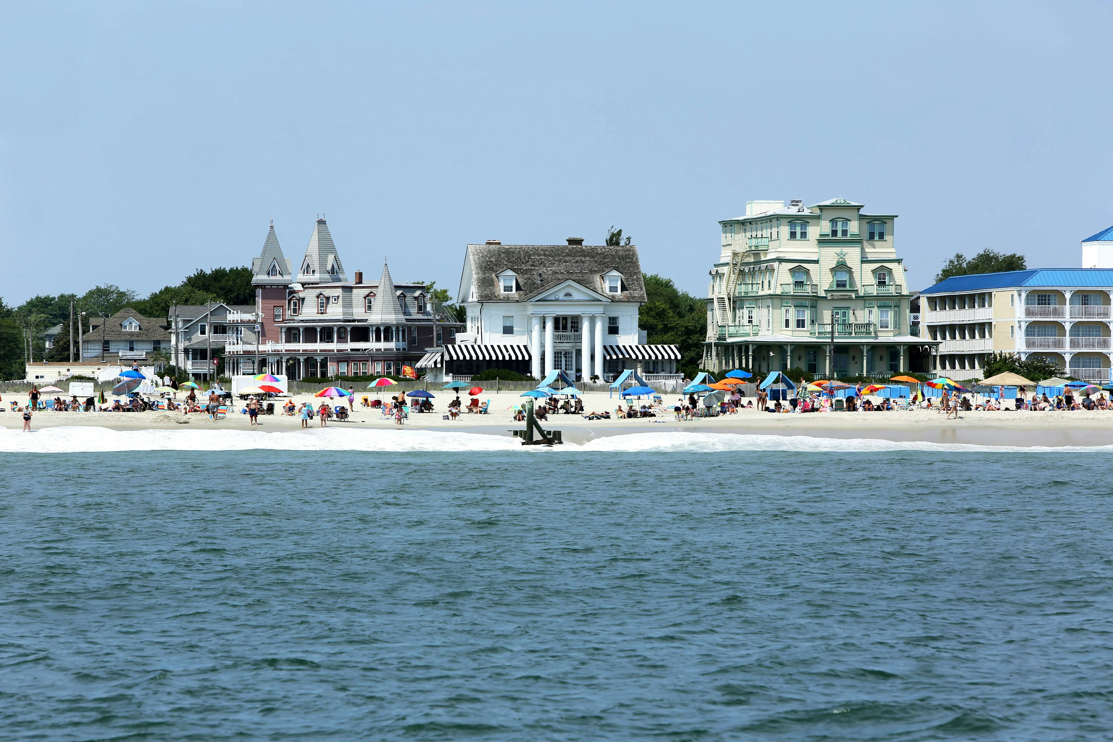 A shot of the shoreline taken from out at sea, showing Victorian buildings lining a beach filled with colorful umbrellas