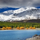 A distant kayaker paddles past a snow-capped mountainous landscape near Lake Tekapo.
295213541
hill, island, snowy, destination, shore, green, autumn, travel, serenity, view, lakeside, new, seasonal, mountains, yellow, south, bright, canoe, scenery, grass, lake, clarity, alps, clouds, southern, season, kayak, bush, range, forest, highlands, fall, blue, panorama, outdoors, sky, boat, scenic, tourism, beautiful, snow, water, nature, mackenzie, environment, canterbury, landscape, tekapo, zealand