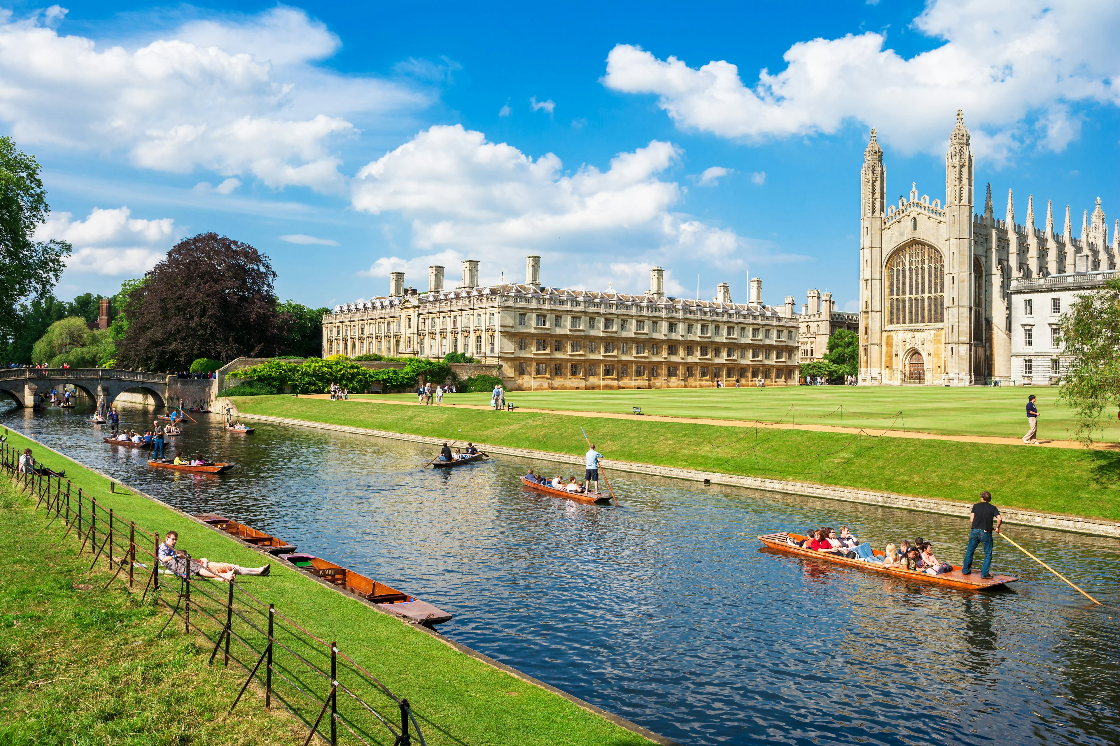 People on small flat-bottomed boats travel along a river lined by fields with large grand buildings