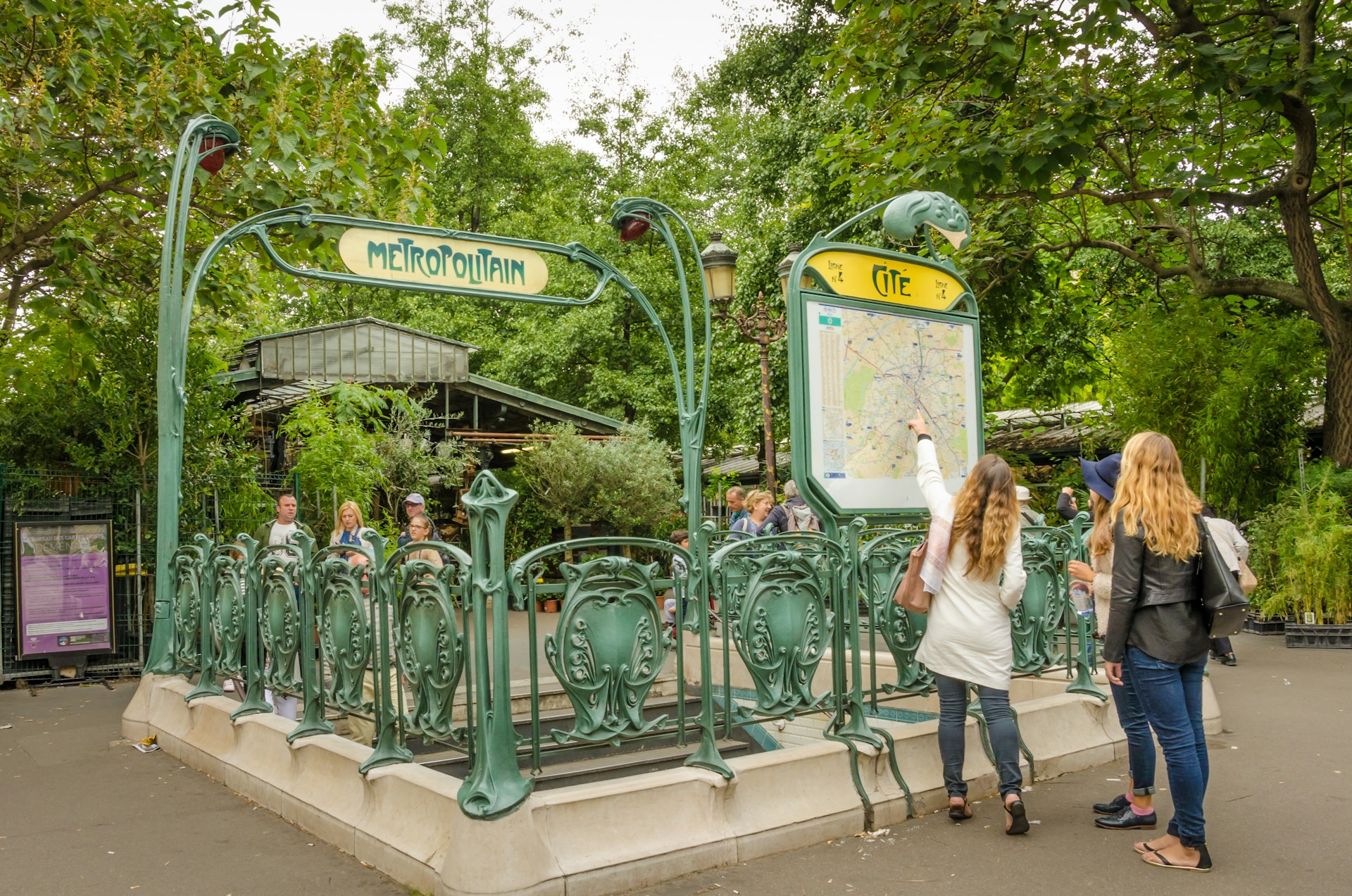 Two girls examine map outside the Cite Metro station which has retained its original Art Nouveau sculpted entrance designed by architect Hector Guimard.