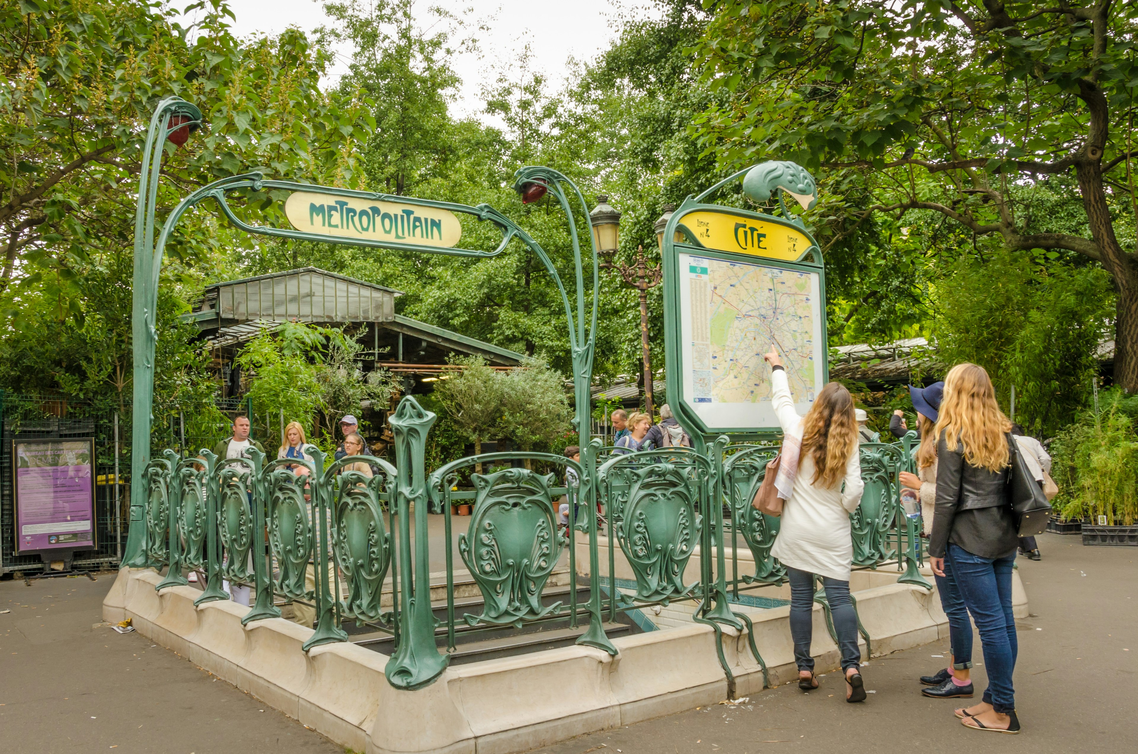 Two girls examine map outside the Cite Metro station which has retained its original Art Nouveau sculpted entrance designed by architect Hector Guimard.