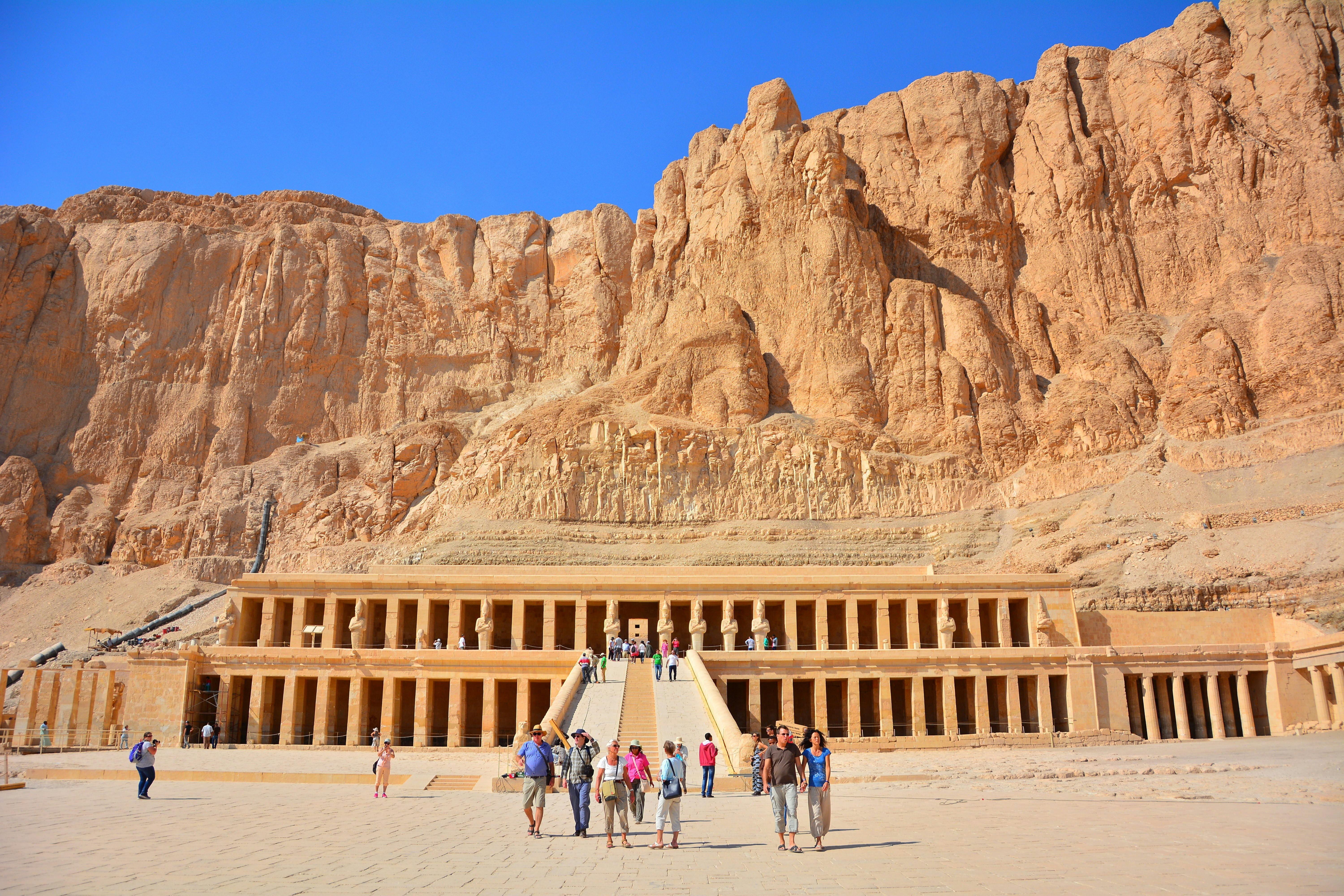 People wander in front of a vast columned temple built into a rocky hill