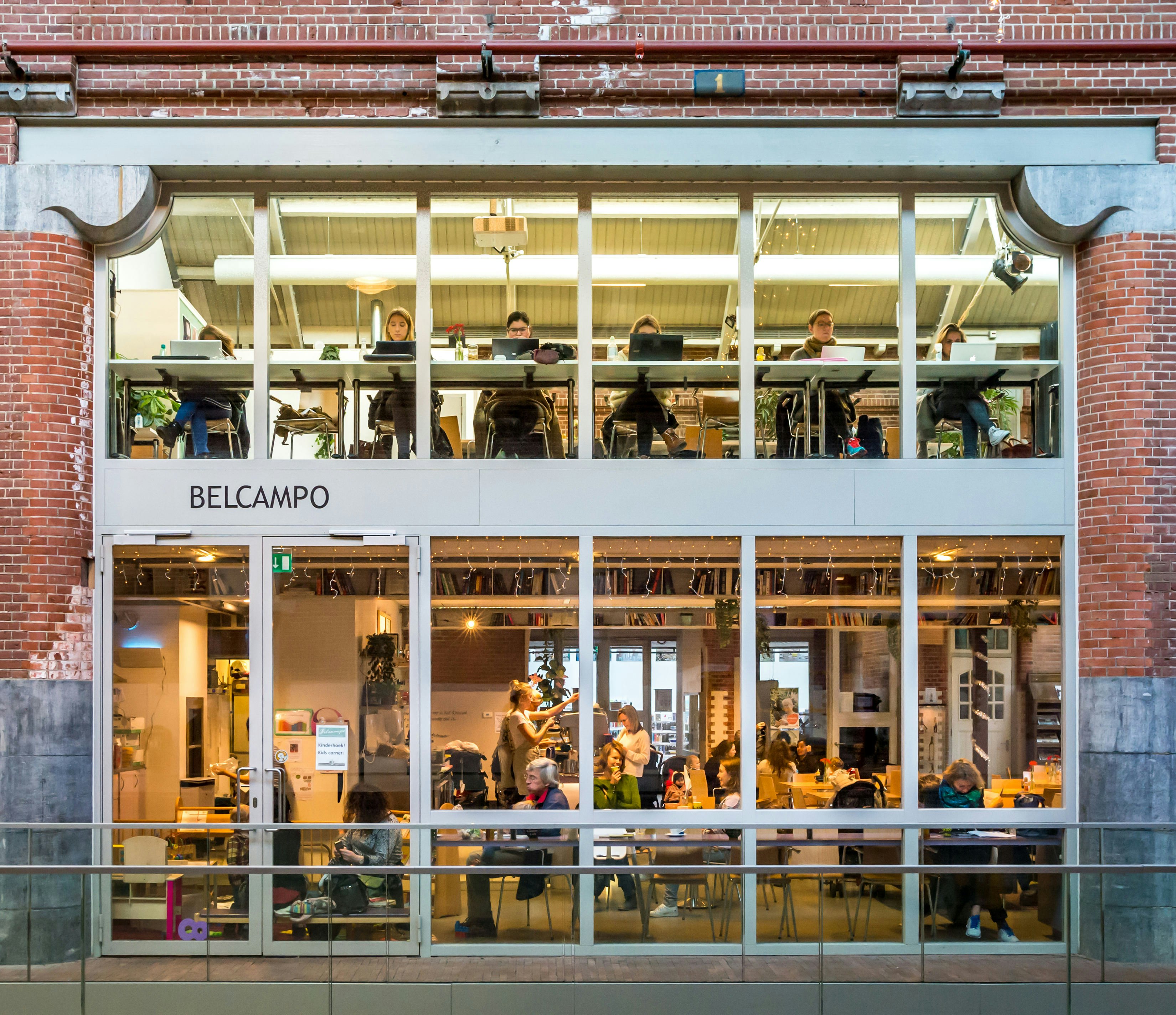 A large series of windows in a former industrial building with people inside sat at laptops or tables