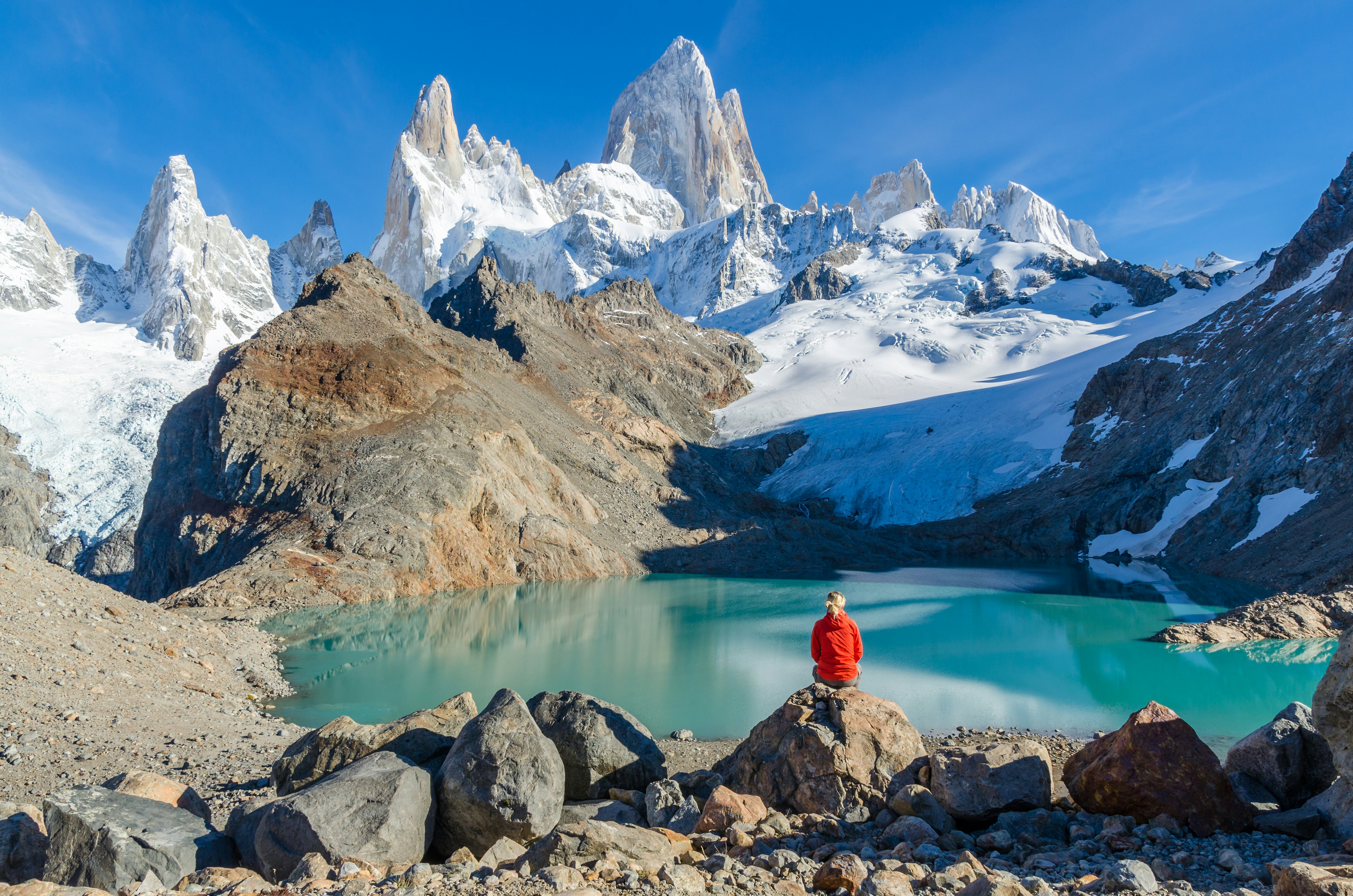 Woman sitting on a rock and admiring Mount Fitz Roy, a rocky Patagonian range.