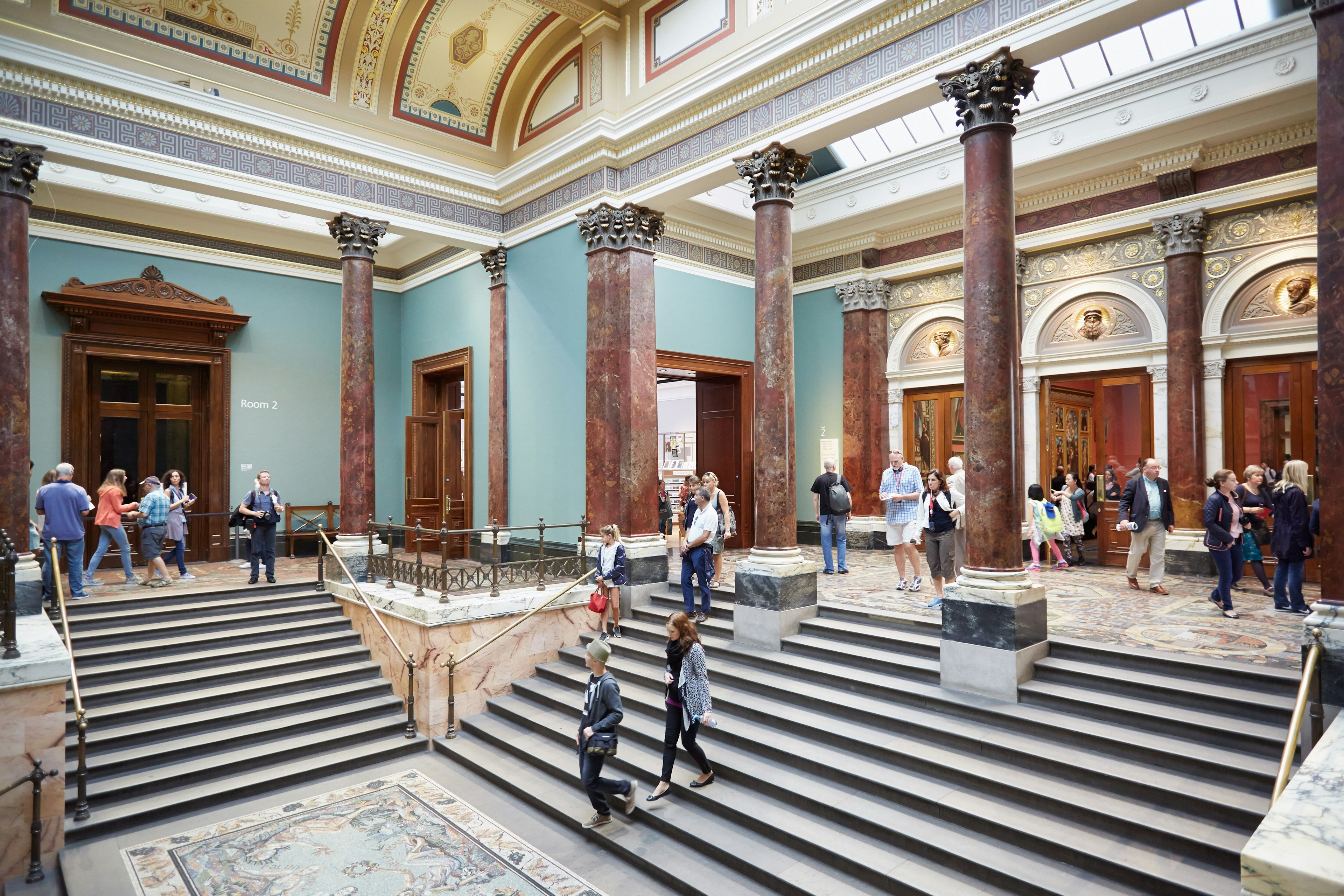 Visitors in the National Gallery going down stairs lined with columns