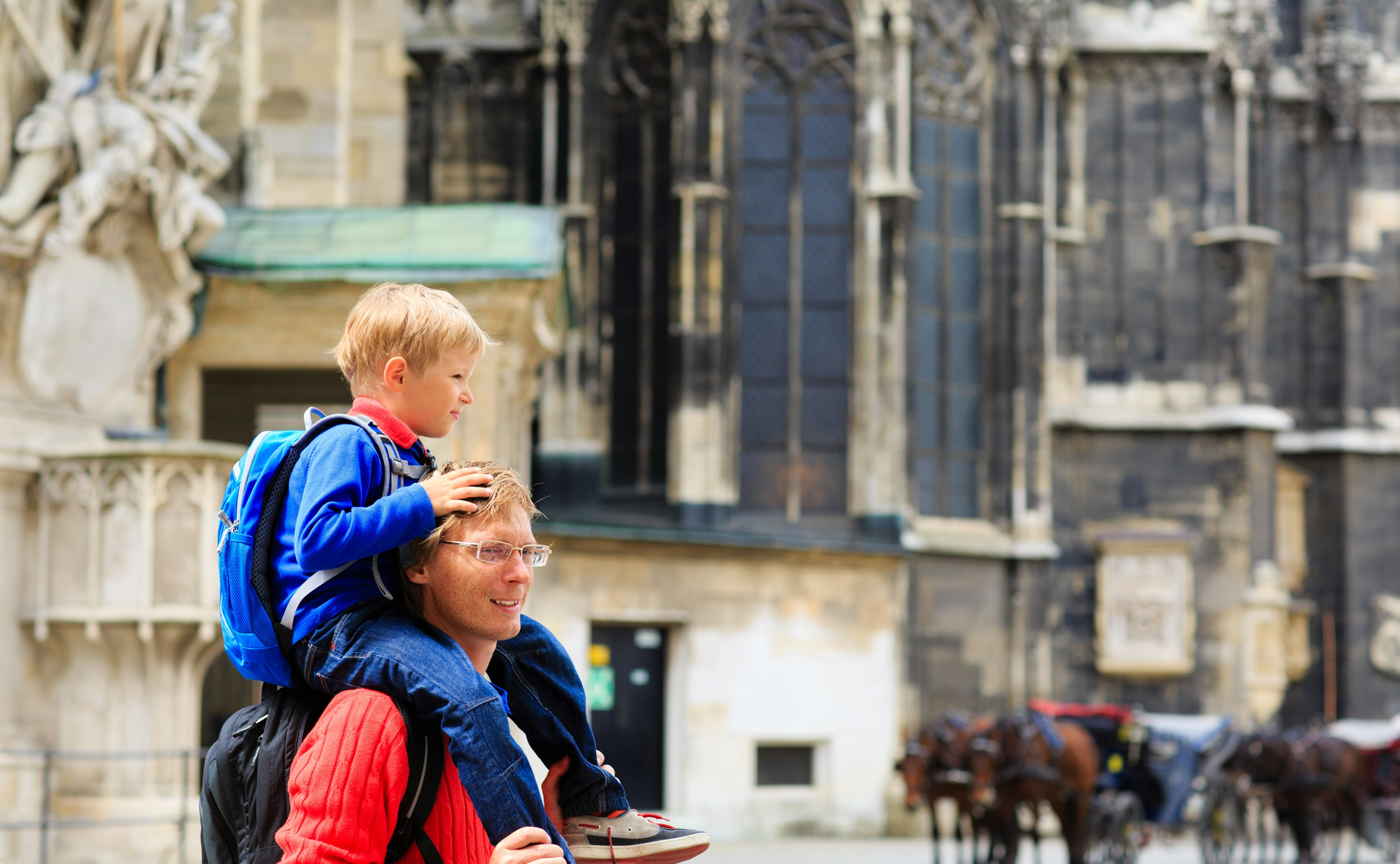 A young blonde boy on the shoulders of this father walk around Vienna near the Stephansdom Catherdal