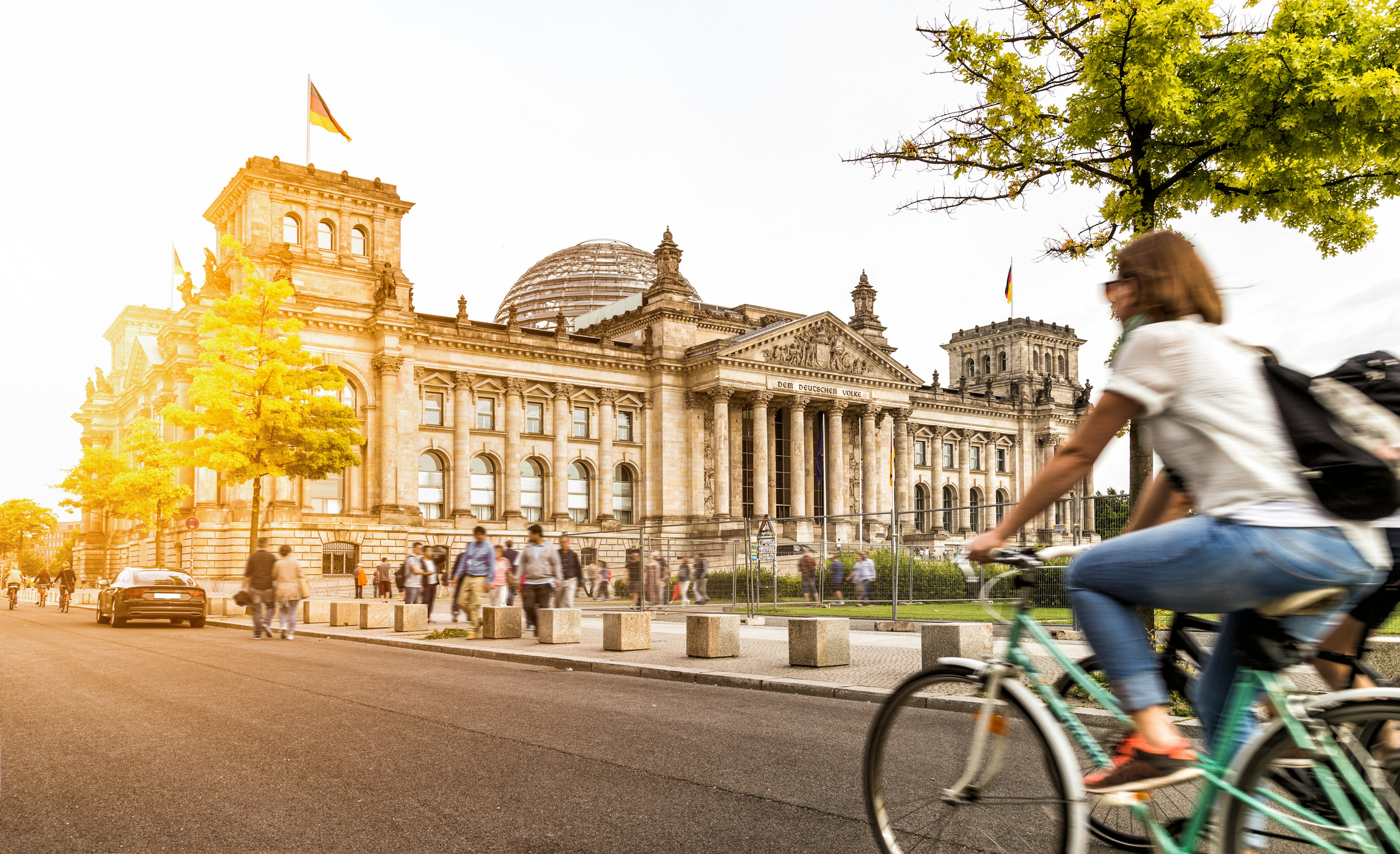 Two people ride bikes on the road, passing a large government building, the Reichstag, in Berlin