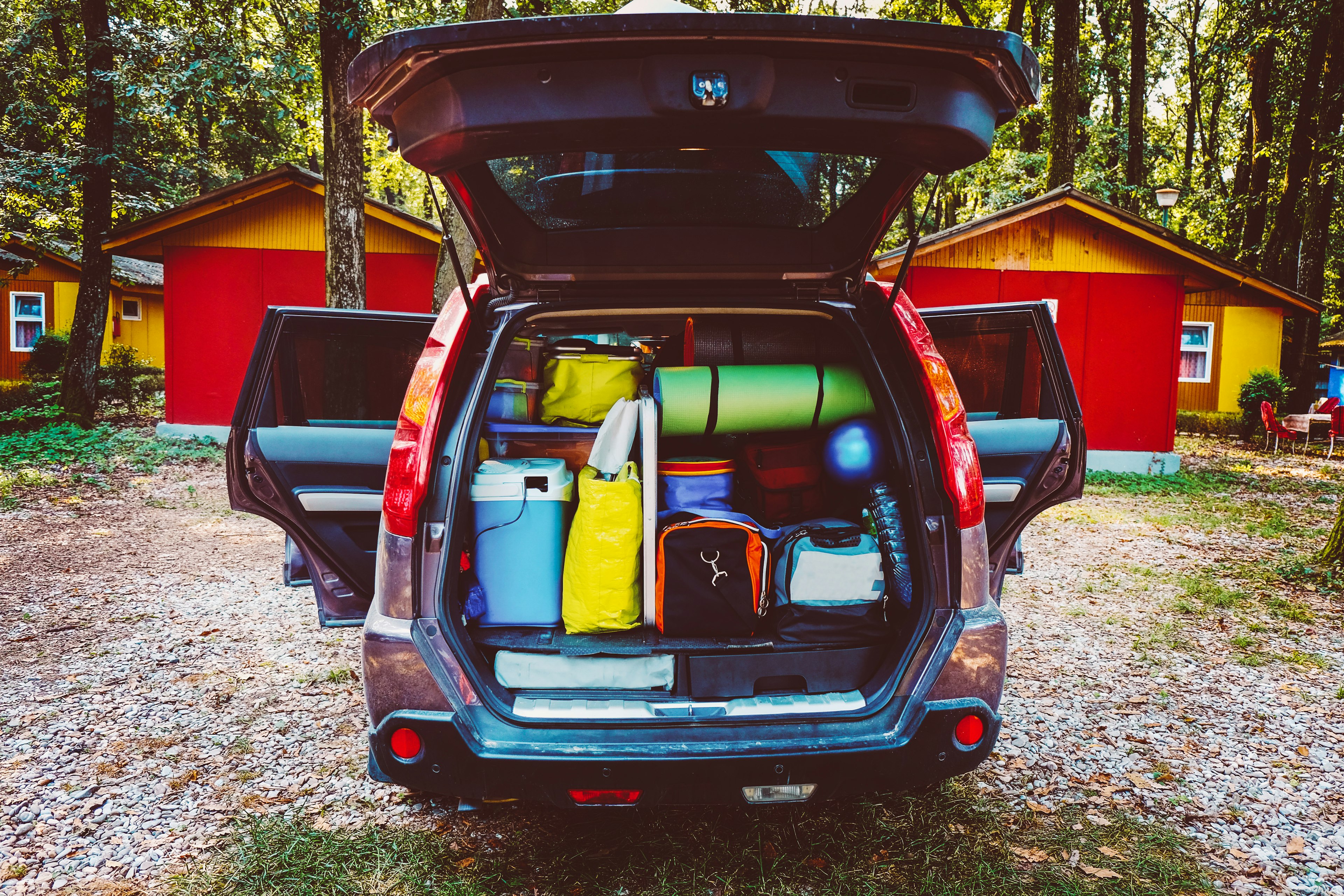 Camping luggage tightly packed into a car trunk in a forest setting.