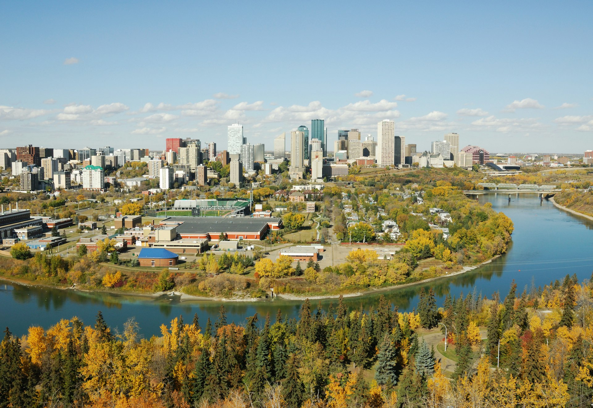 A city with several high-rise buildings on the edge of a river surrounded by greenery