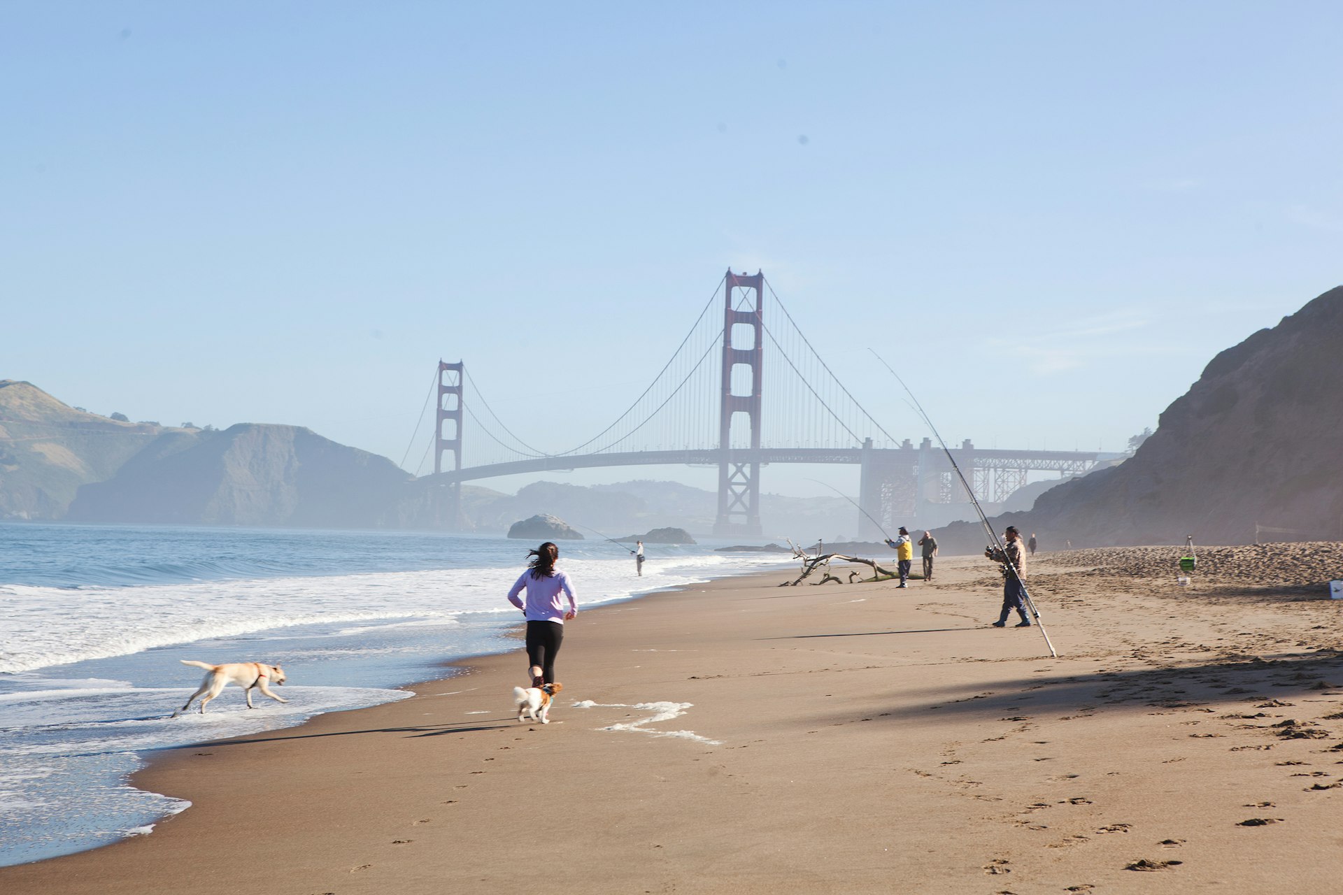 People running and fishing on Baker Beach with the Golden Gate bridge in the background