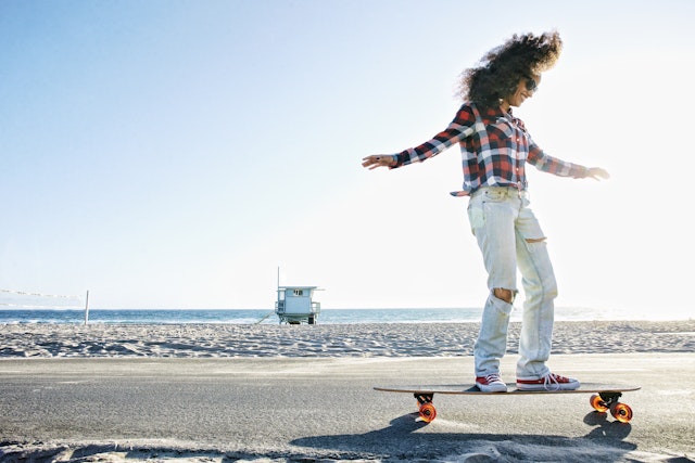 Hispanic woman riding skateboard at beach