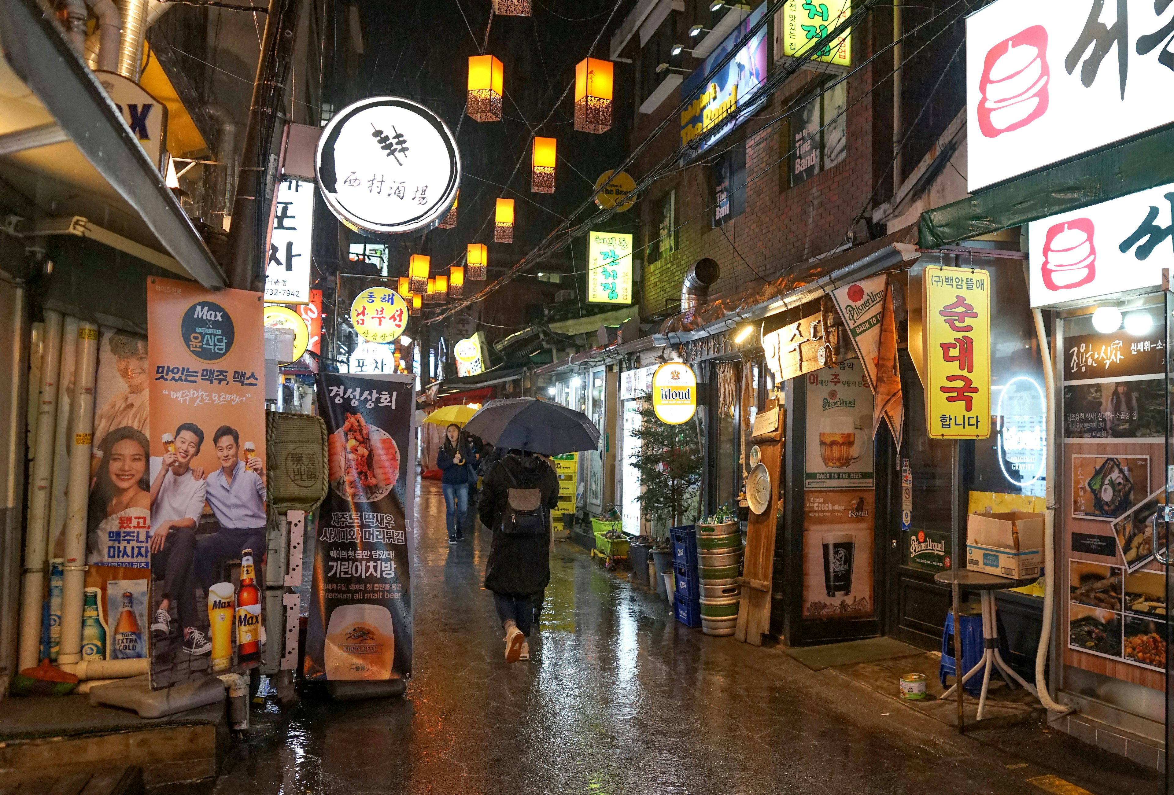 People walk under umbrellas by lit street signs on a rainy night in Tongin-dong, Seoul, South Korea