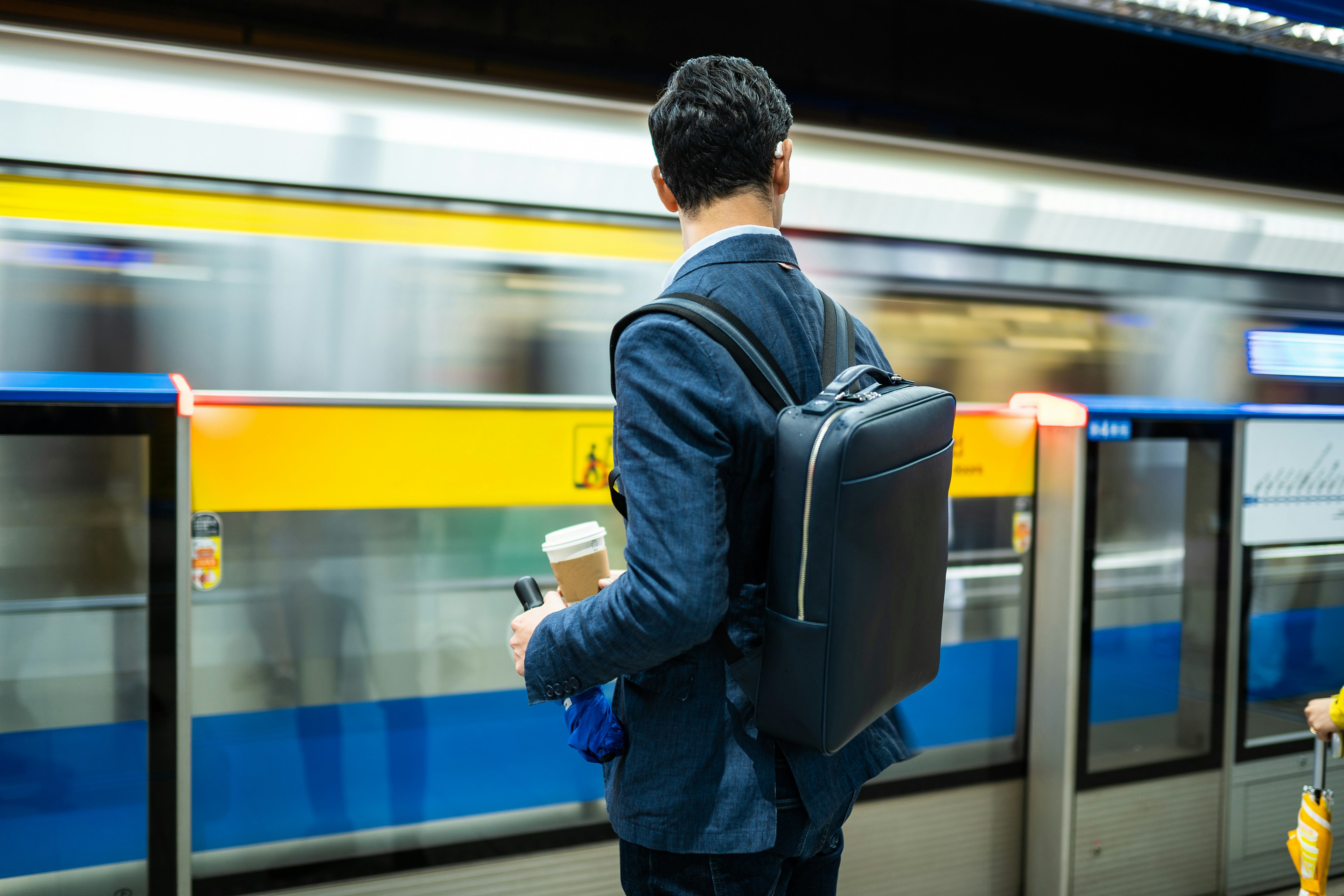 Rear view of a man waiting for a subway train, holding a bag on his back and cup of coffee in Taipei